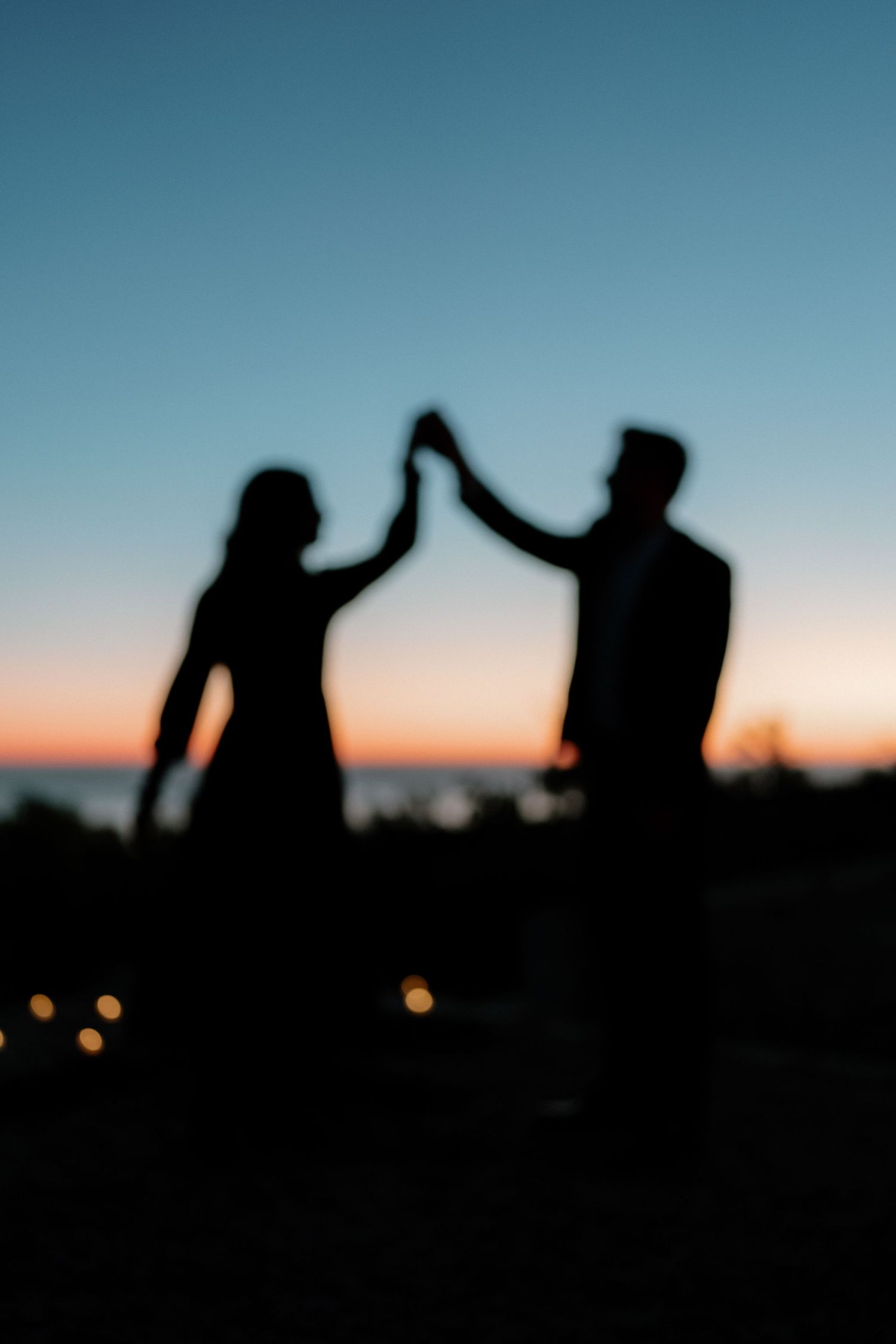 Silhouette of a couple dancing and holding hands against a vibrant sunset sky at dusk.