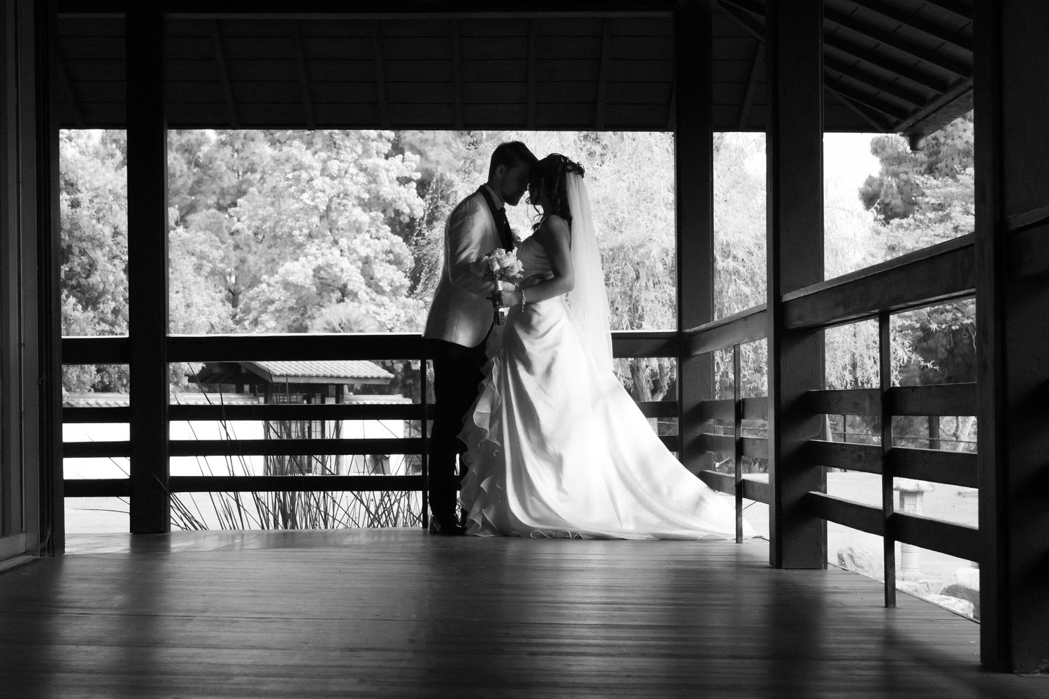 Black and white wedding photo of bride and groom sharing a romantic kiss on a wooden pavilion bridge.