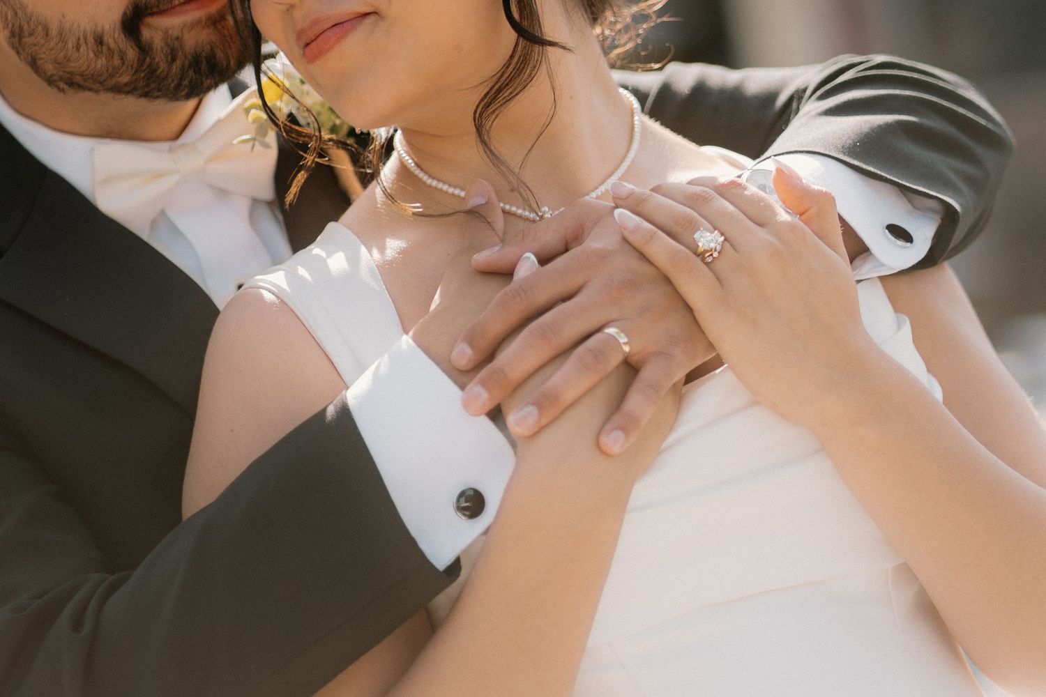 Bride and groom embracing, showcasing diamond engagement ring and wedding band with elegant white gown and suit cufflinks.