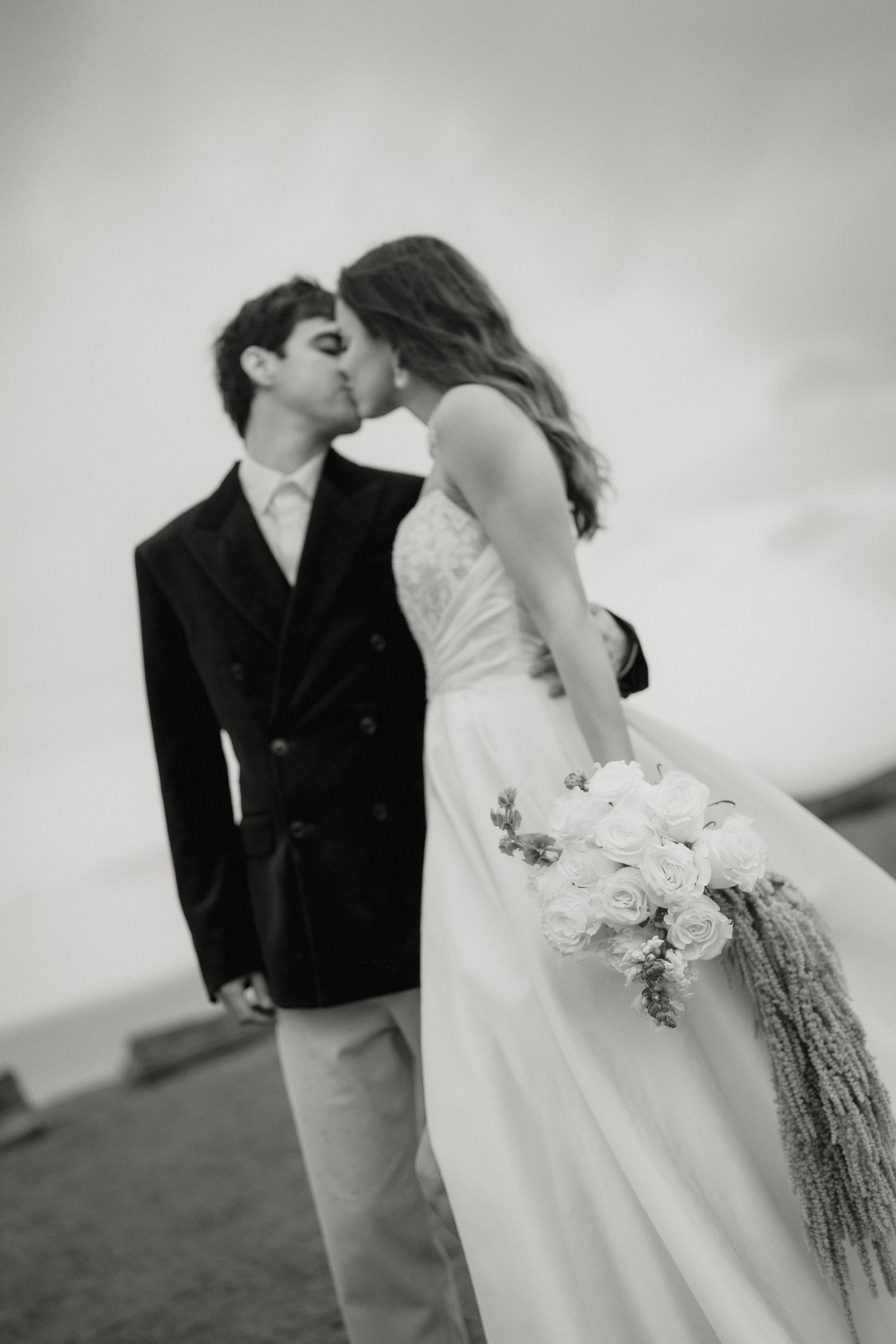 Black and white photo of bride and groom sharing a kiss outdoors.