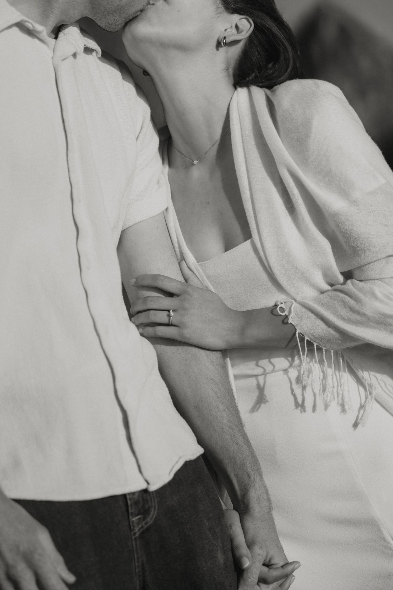 Black and white close-up of couple embracing, woman wearing engagement ring and fringe shawl.