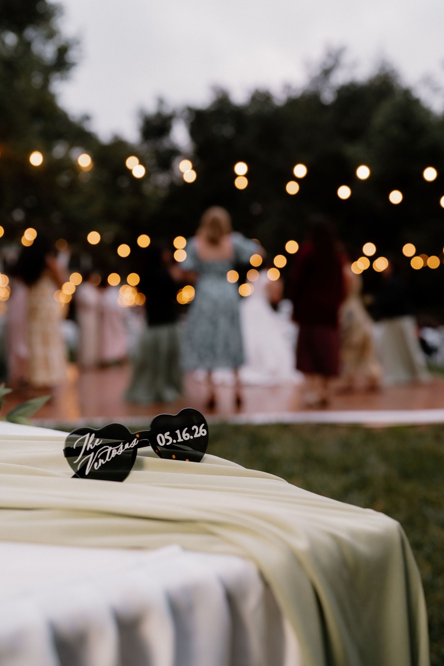 Heart-shaped wedding sunglasses with date 05.16.26 on table at outdoor reception.