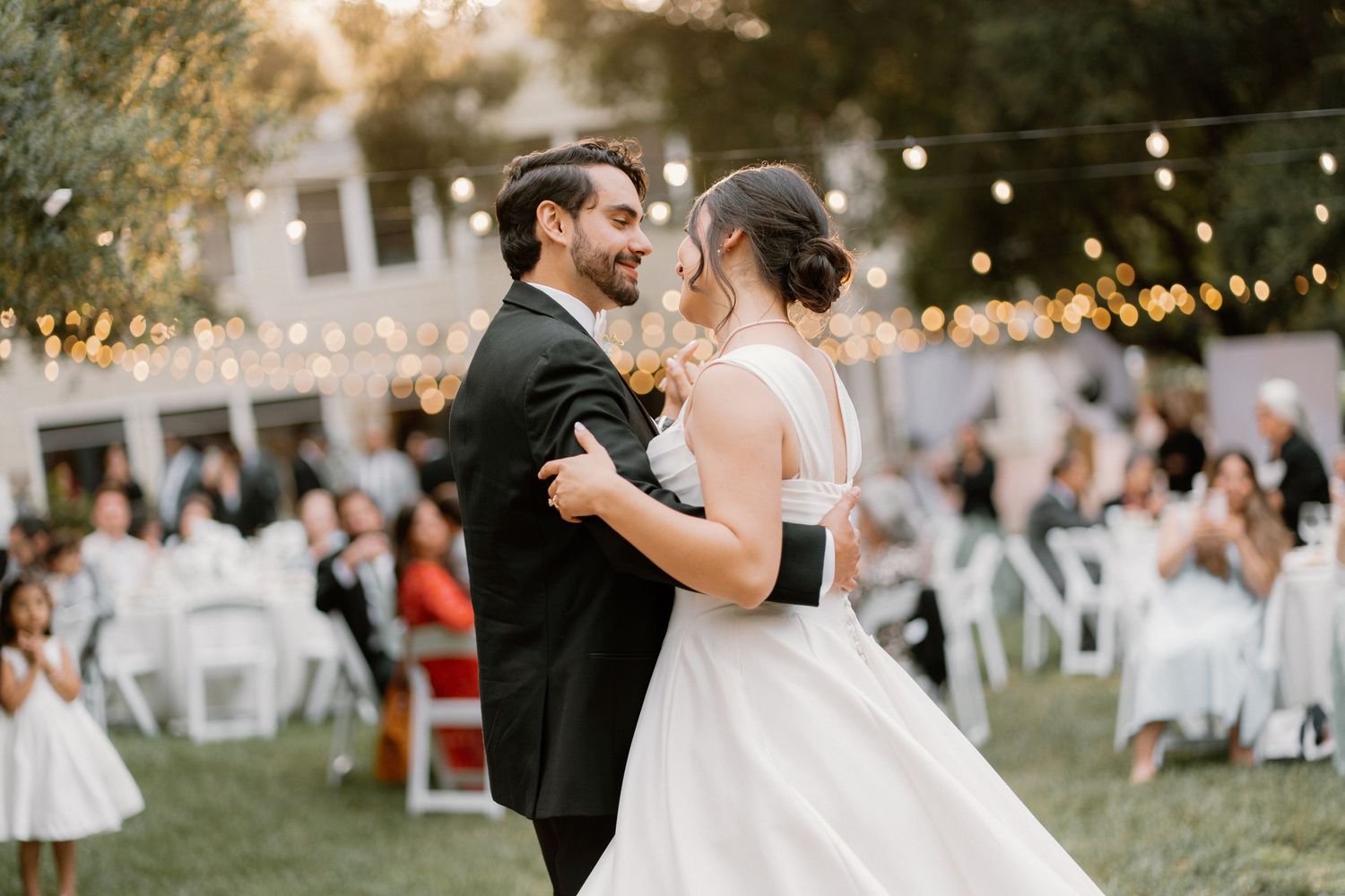 Bride and groom share their first dance under string lights at an outdoor wedding reception.