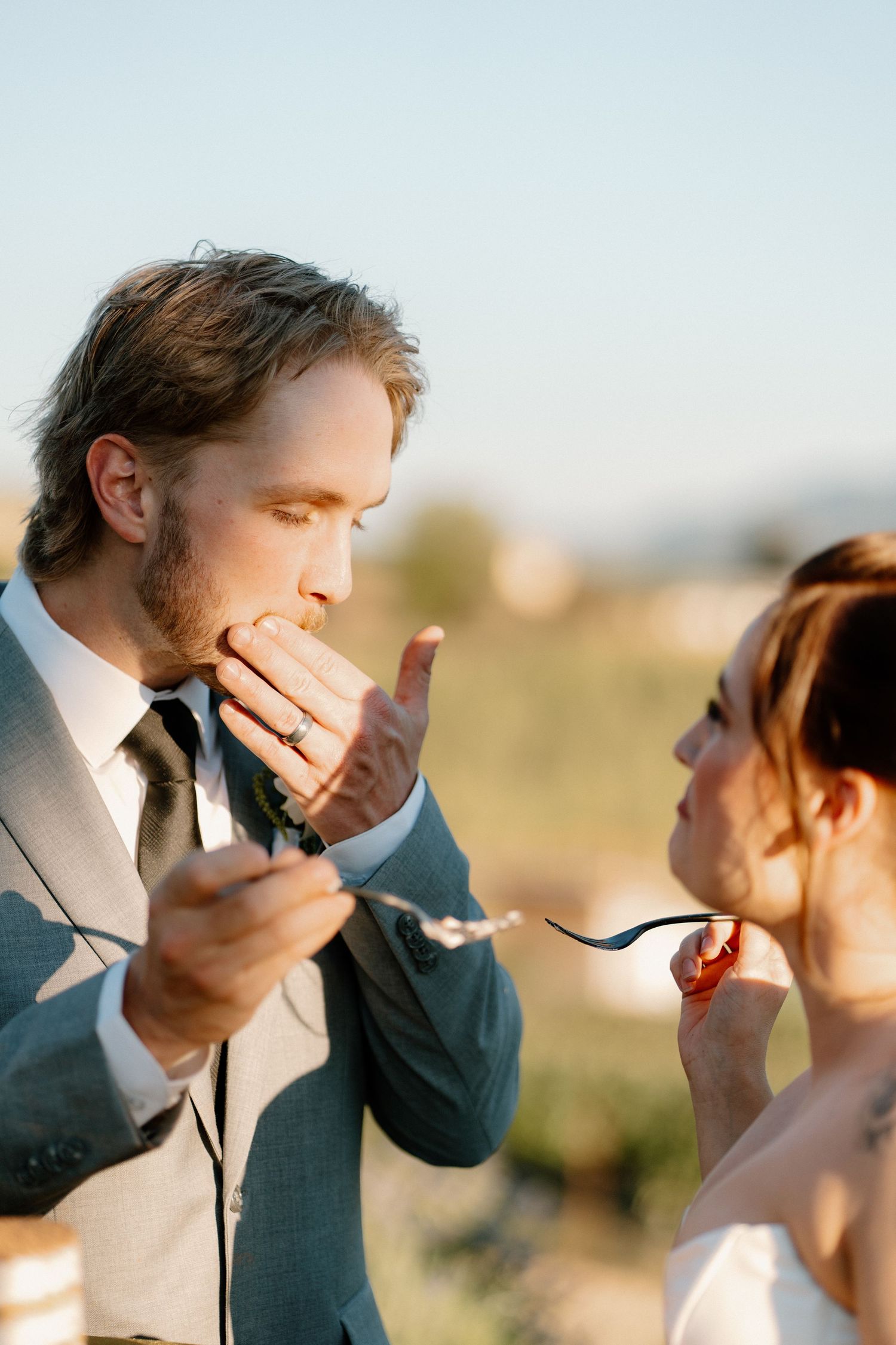 Bride and groom share a playful cake tasting moment outdoors during their golden hour wedding reception.