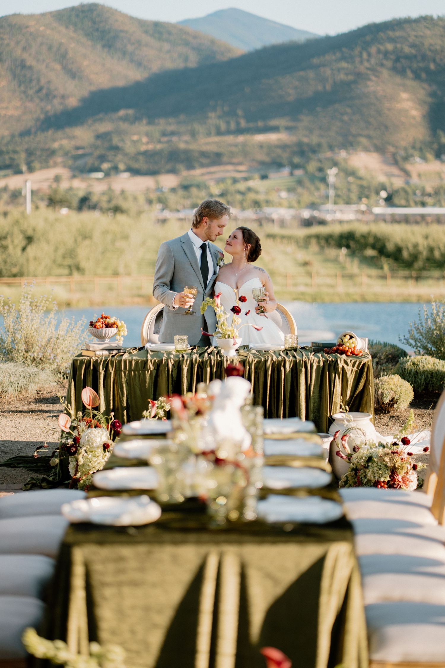 Bride and groom kiss at outdoor sweetheart table with stunning mountain and lake views behind them.