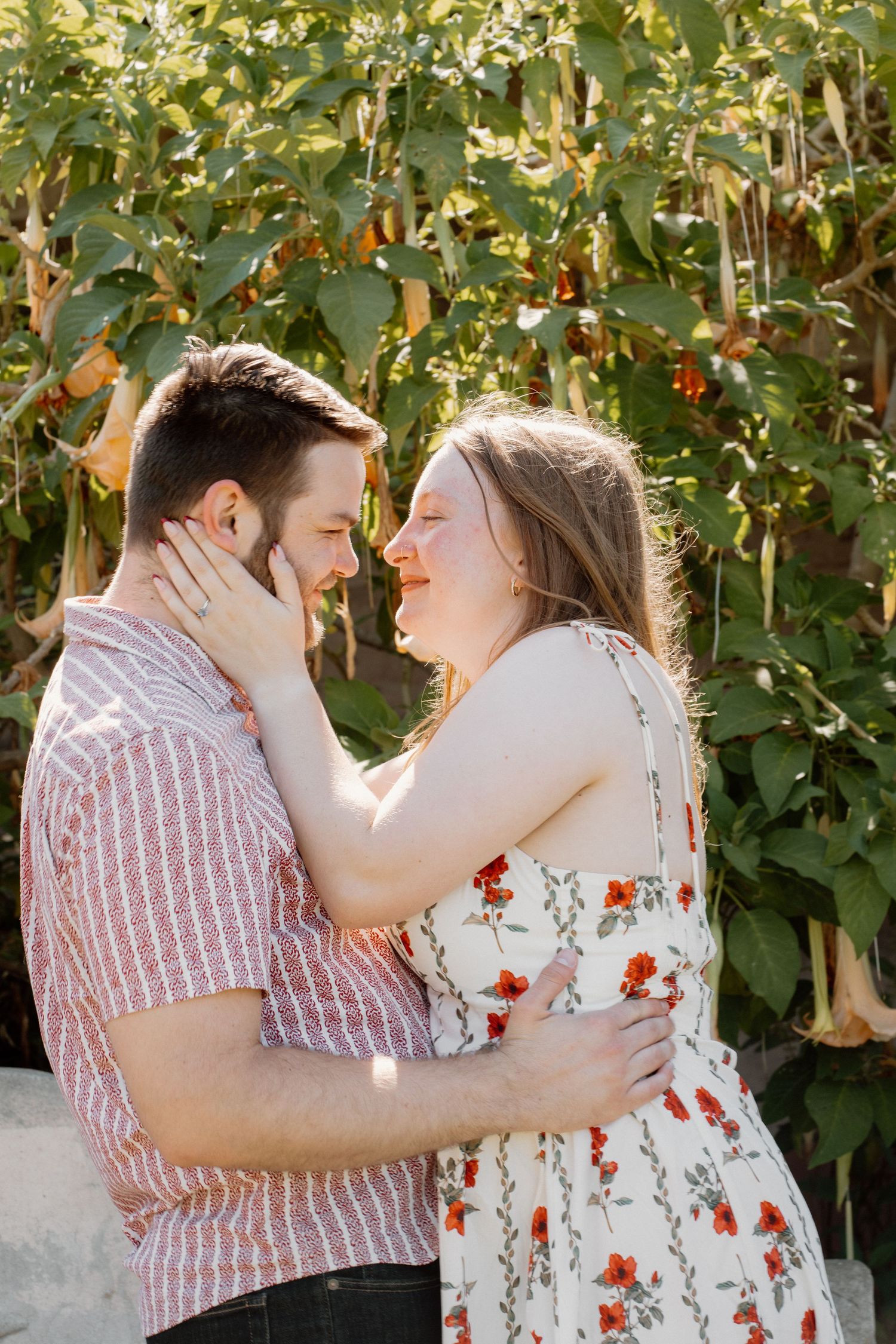 Romantic couple embracing face-to-face outdoors with lush green foliage in the background.