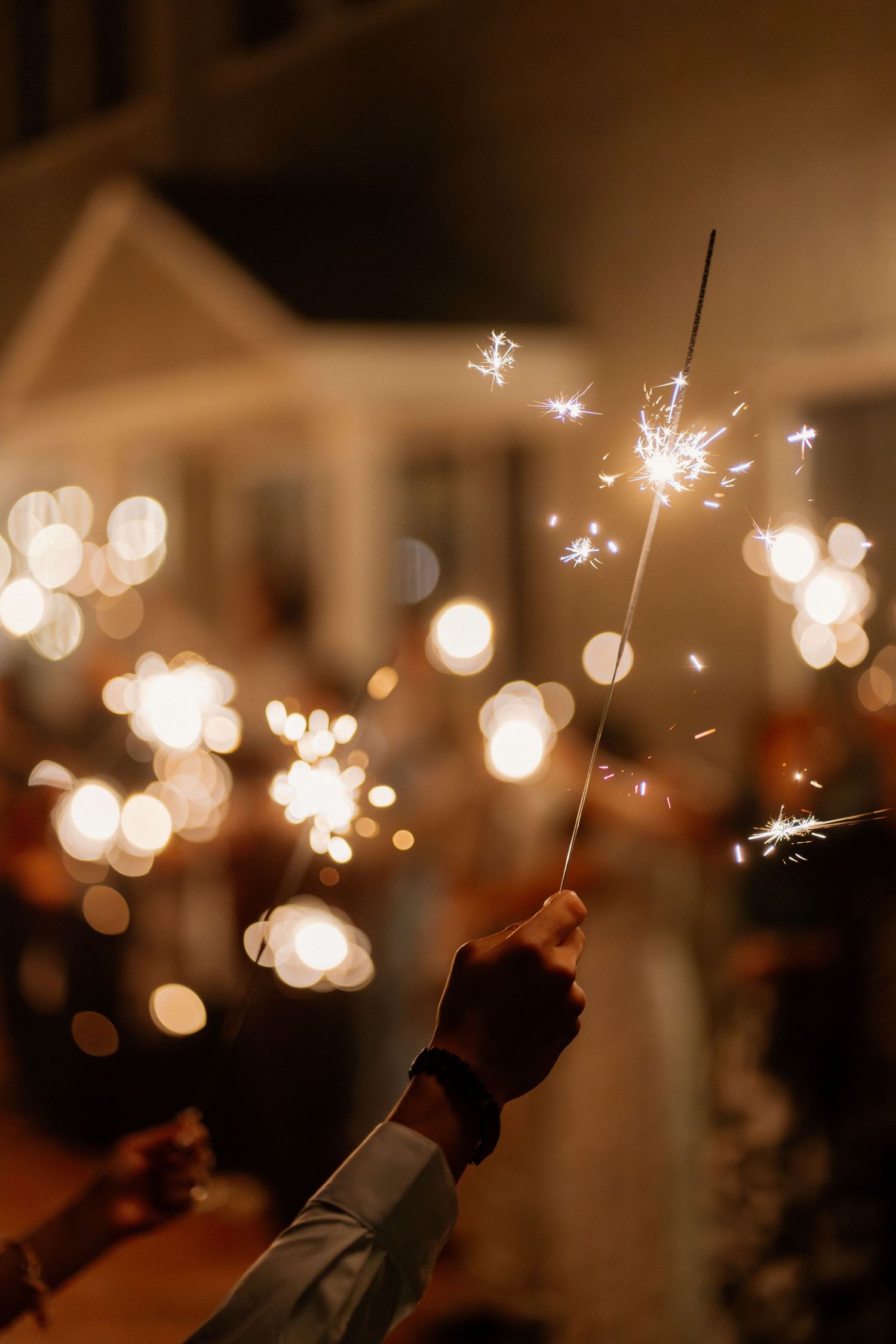 Hand holding a sparkling wedding sparkler during a romantic nighttime sendoff celebration.