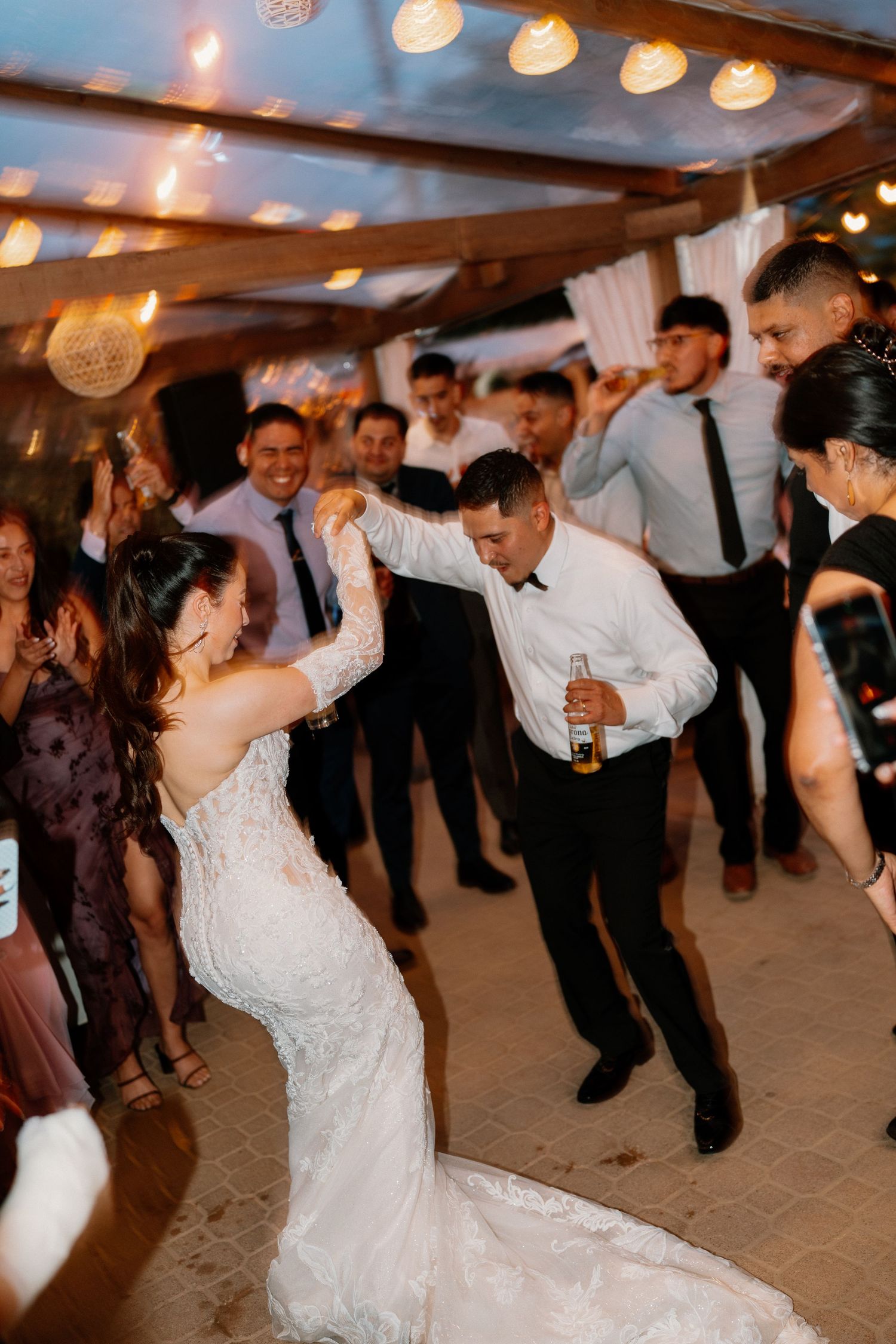 Bride and groom dancing energetically surrounded by cheering guests at their lively wedding reception.