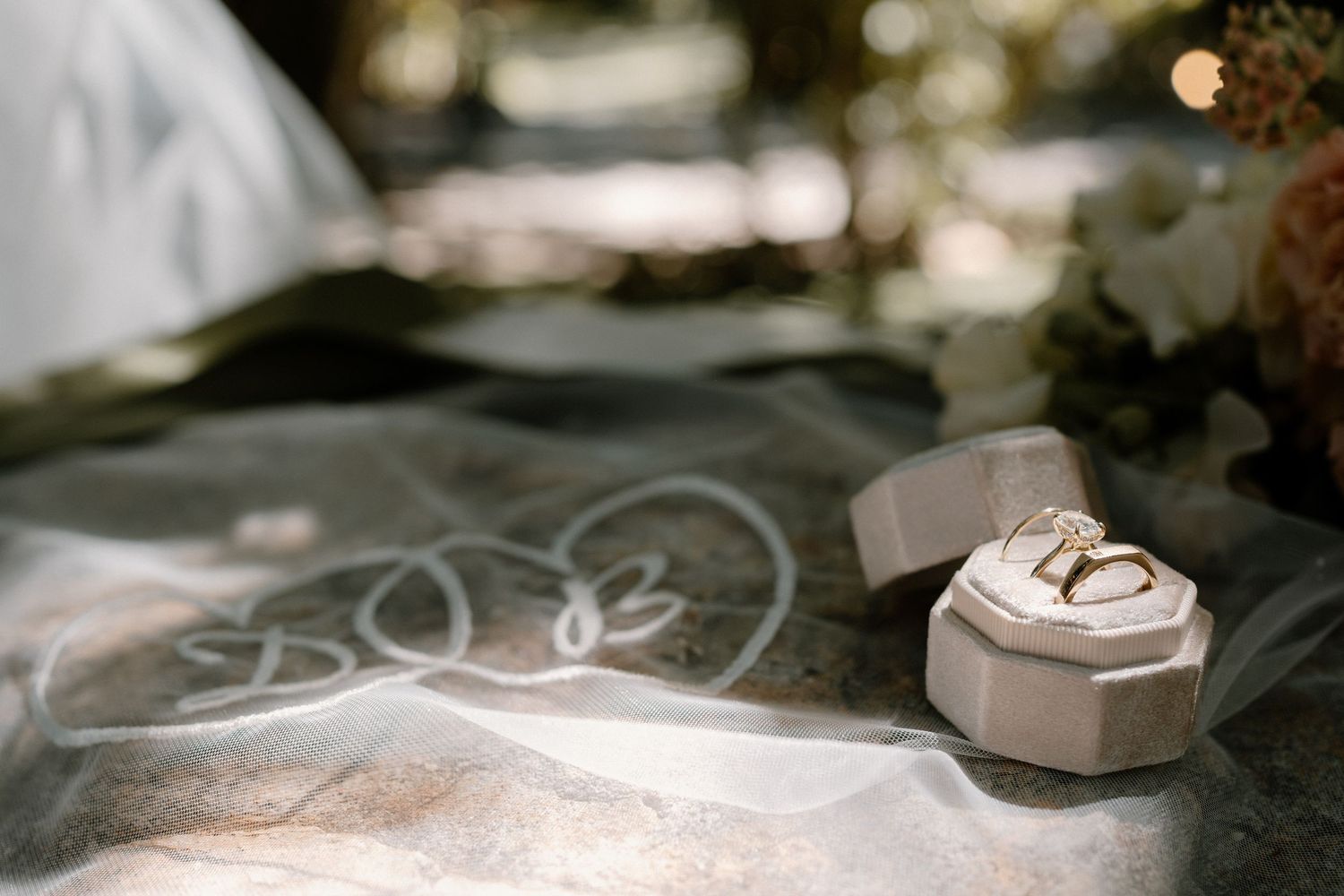 Diamond engagement ring in geometric velvet box displayed on sheer bridal veil with soft bokeh background.