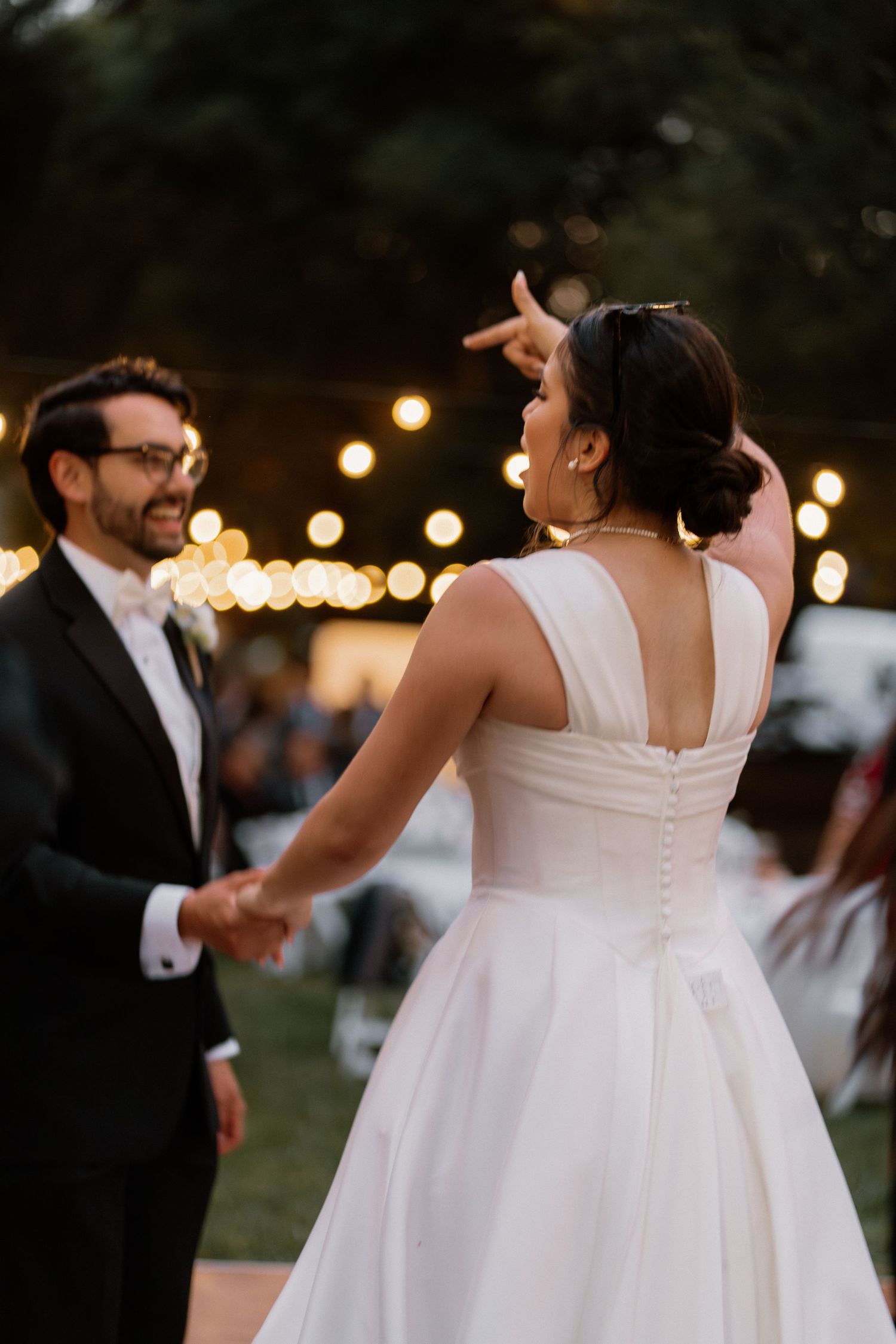 Bride and groom share first dance outdoors under warm string lights at elegant evening wedding reception.