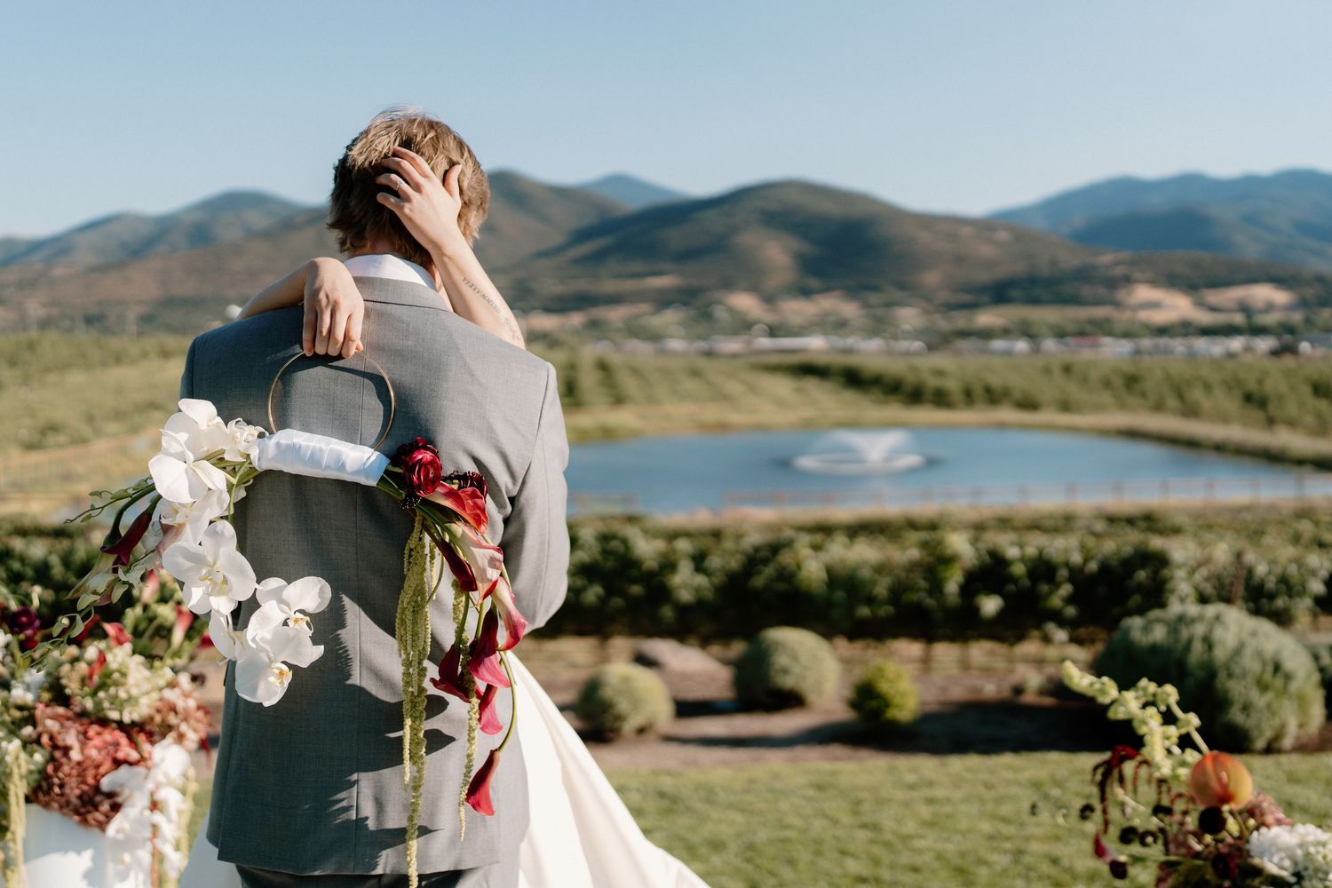 Bride and groom embrace from behind at an outdoor ceremony with a stunning mountain and lake view.
