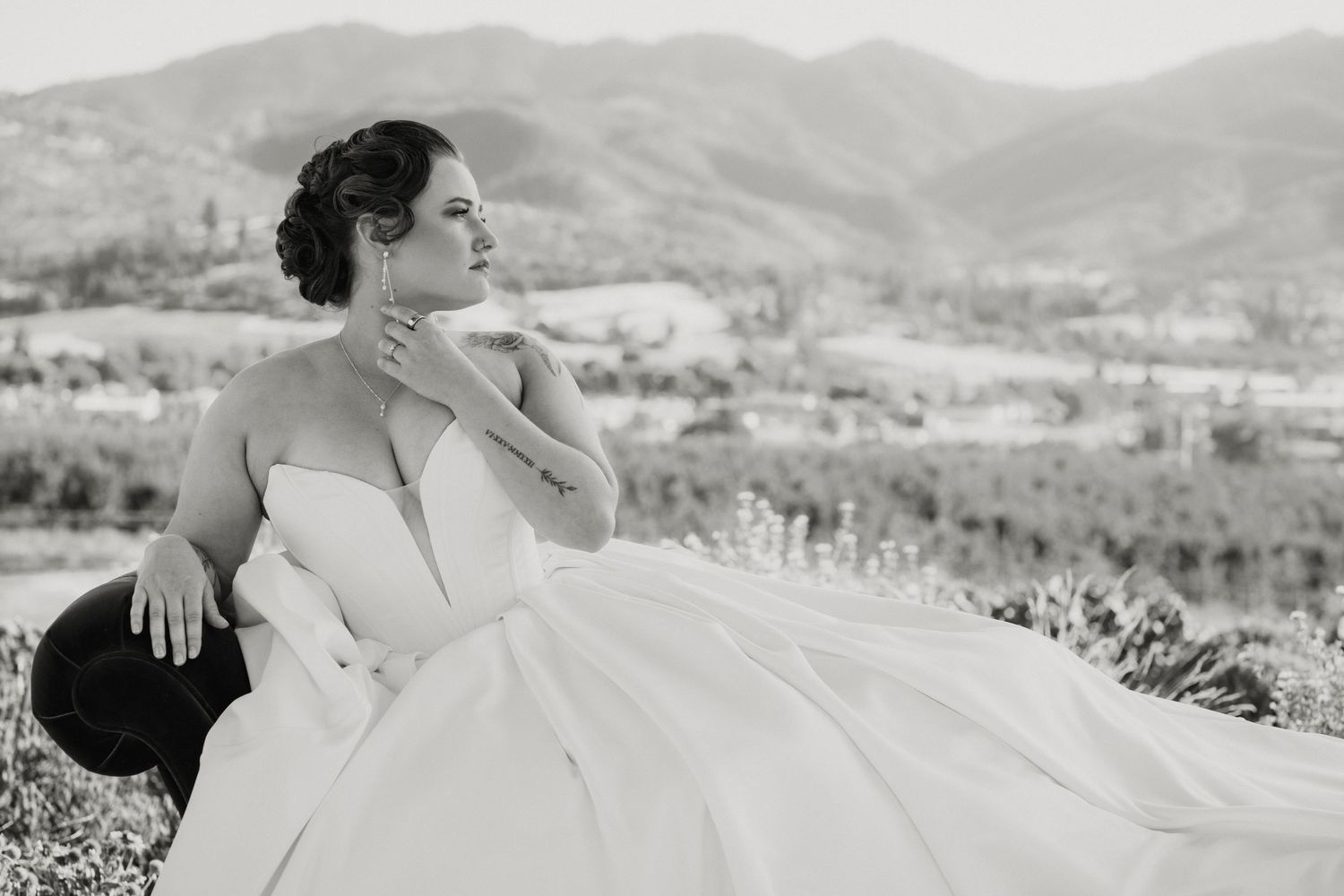 Bride in strapless white ball gown poses gracefully outdoors with scenic mountain valley views in black and white photo.