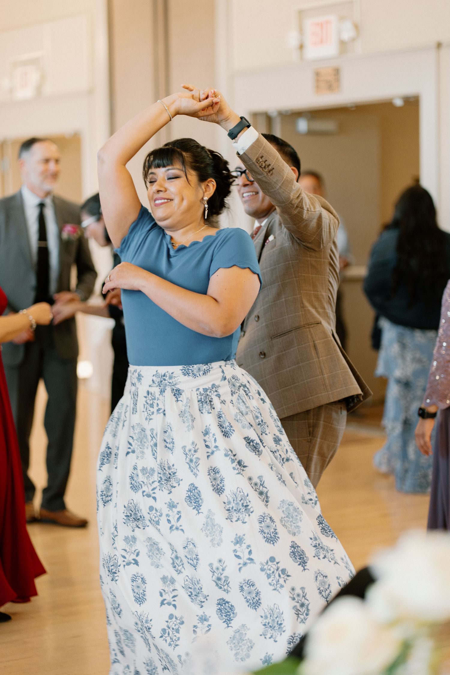 Woman in blue floral skirt being twirled by a partner on a wedding reception dance floor.
