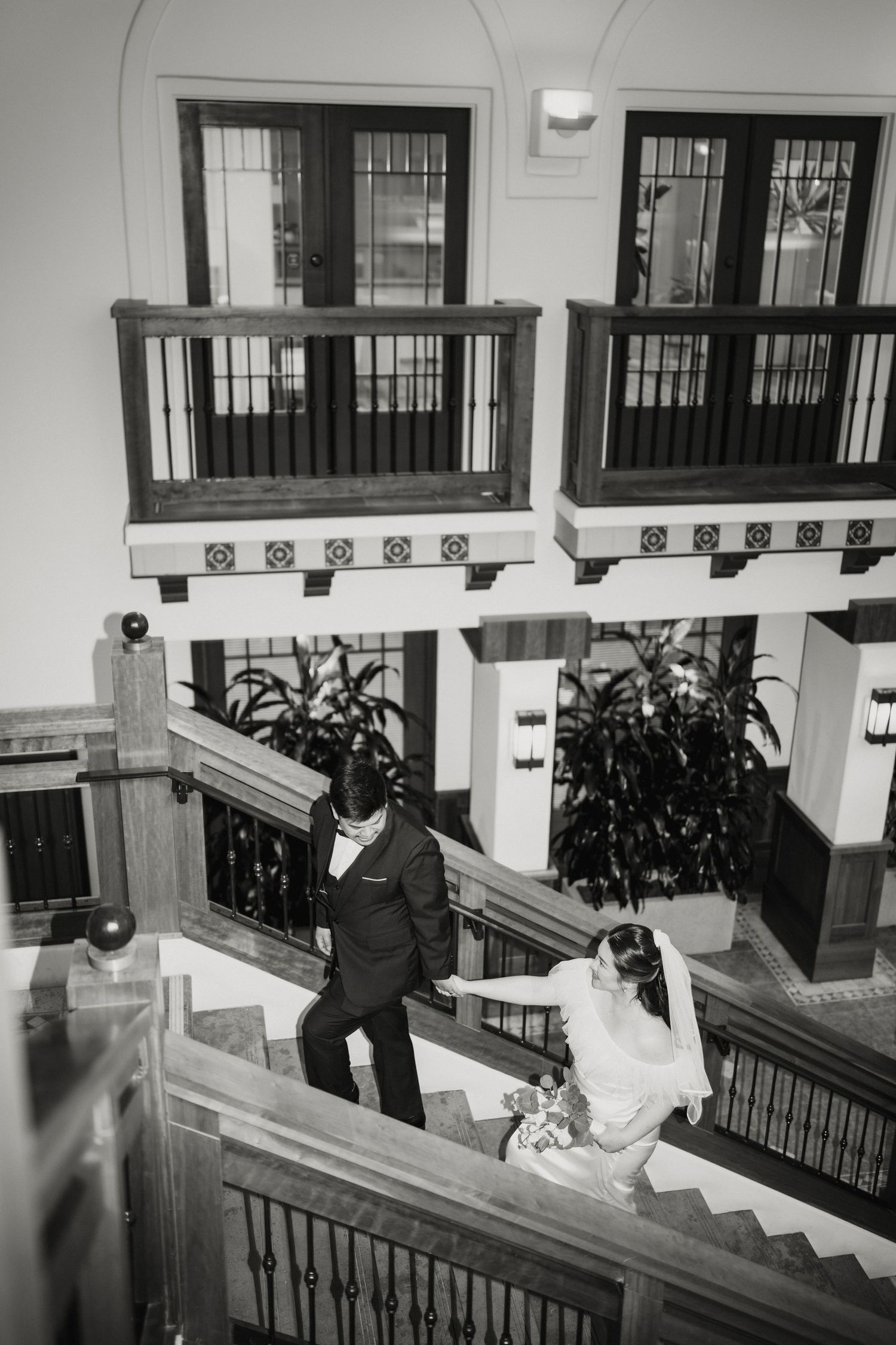 Black and white overhead shot of bride and groom descending an elegant staircase in a historic building.