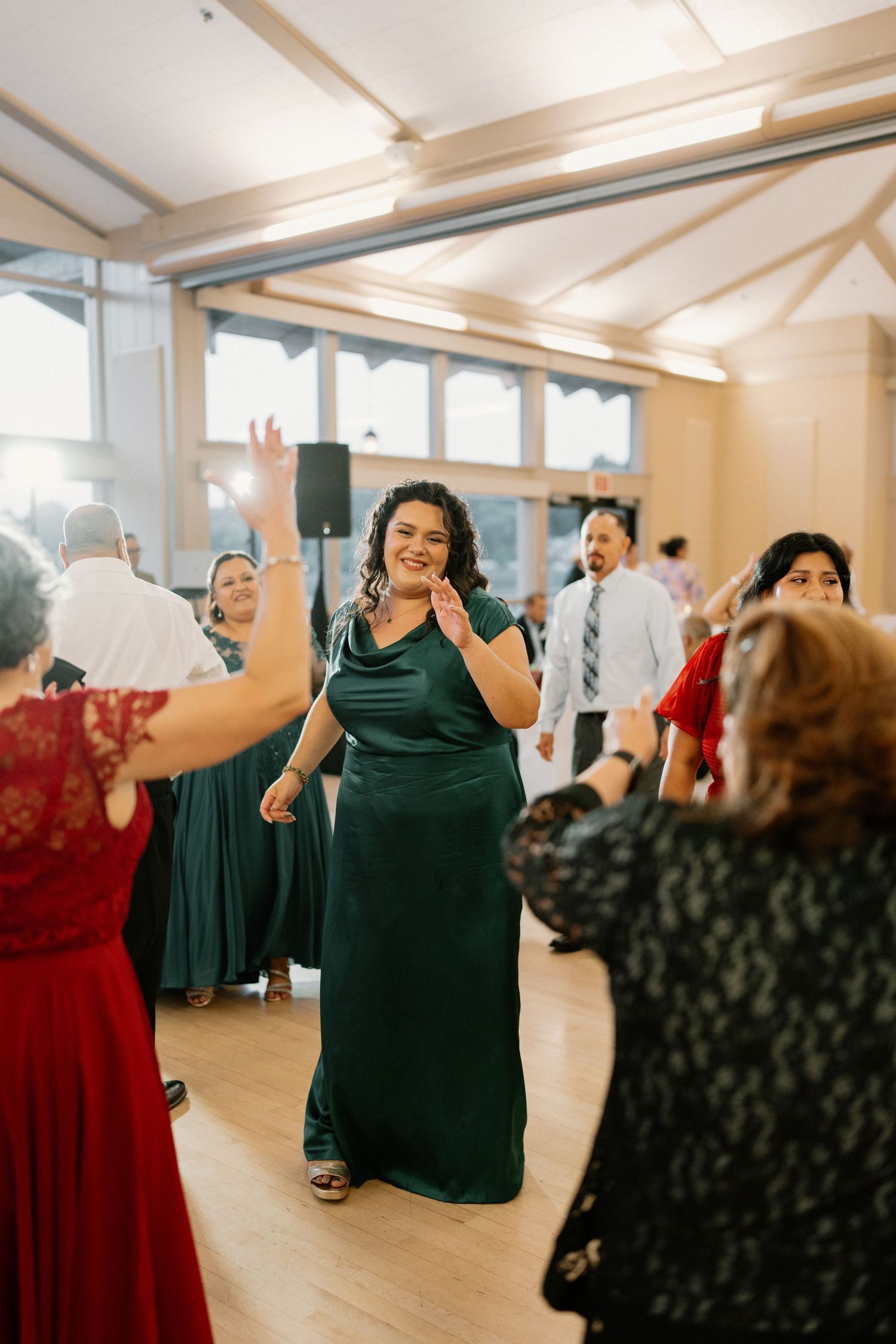 Woman in emerald green gown dancing joyfully surrounded by guests at wedding reception.