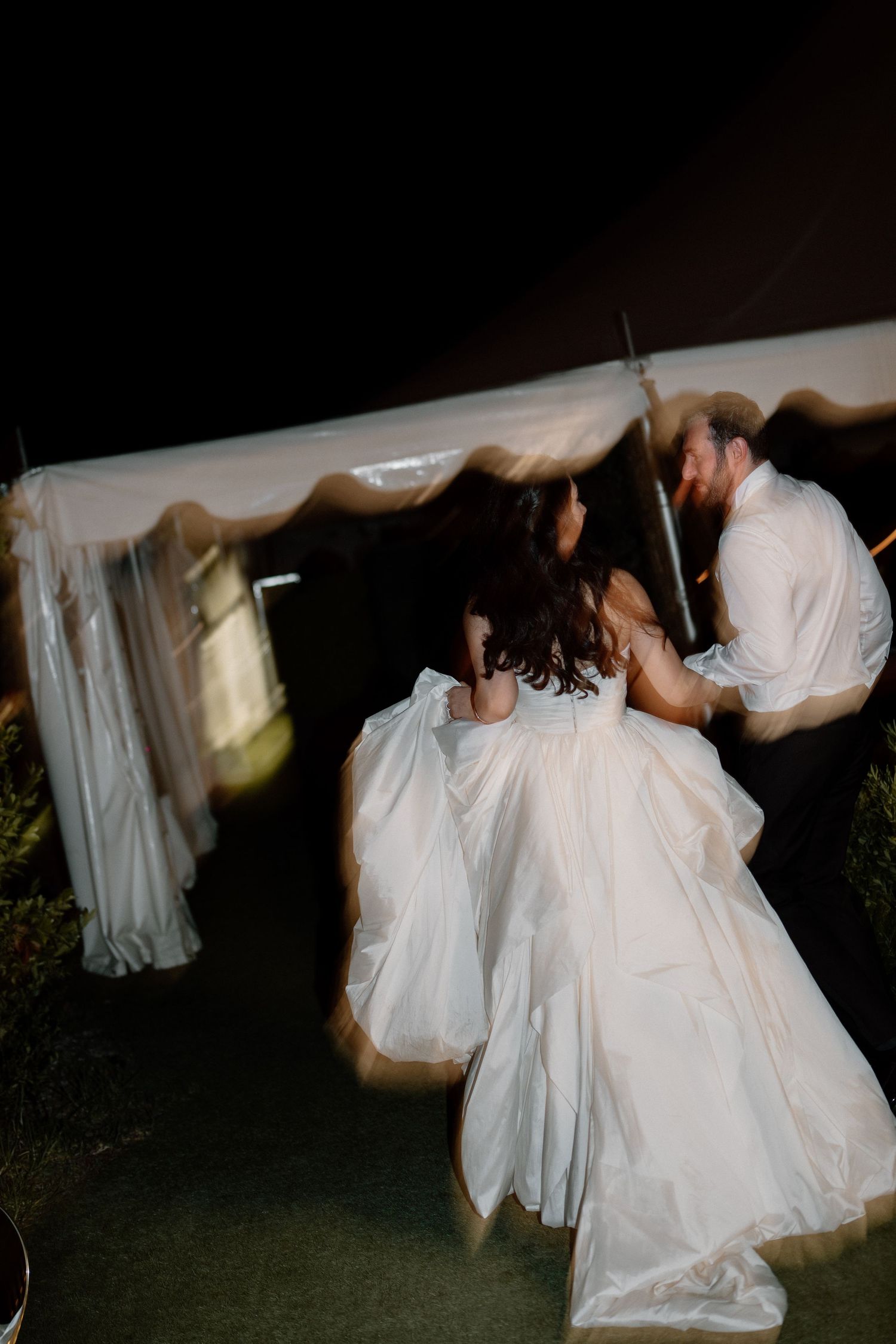 Bride and groom dancing outside a white tent at night during their wedding reception.