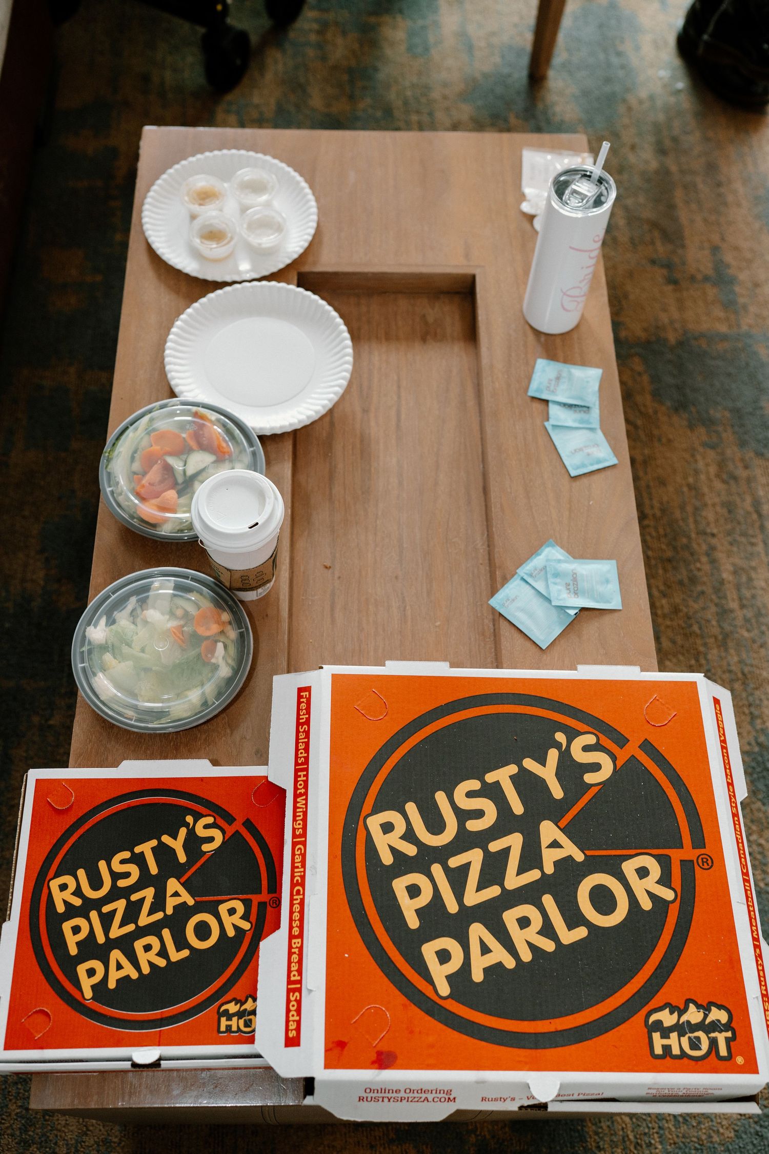 Rusty's Pizza Parlor boxes on wooden table with plates and salads at wedding prep.