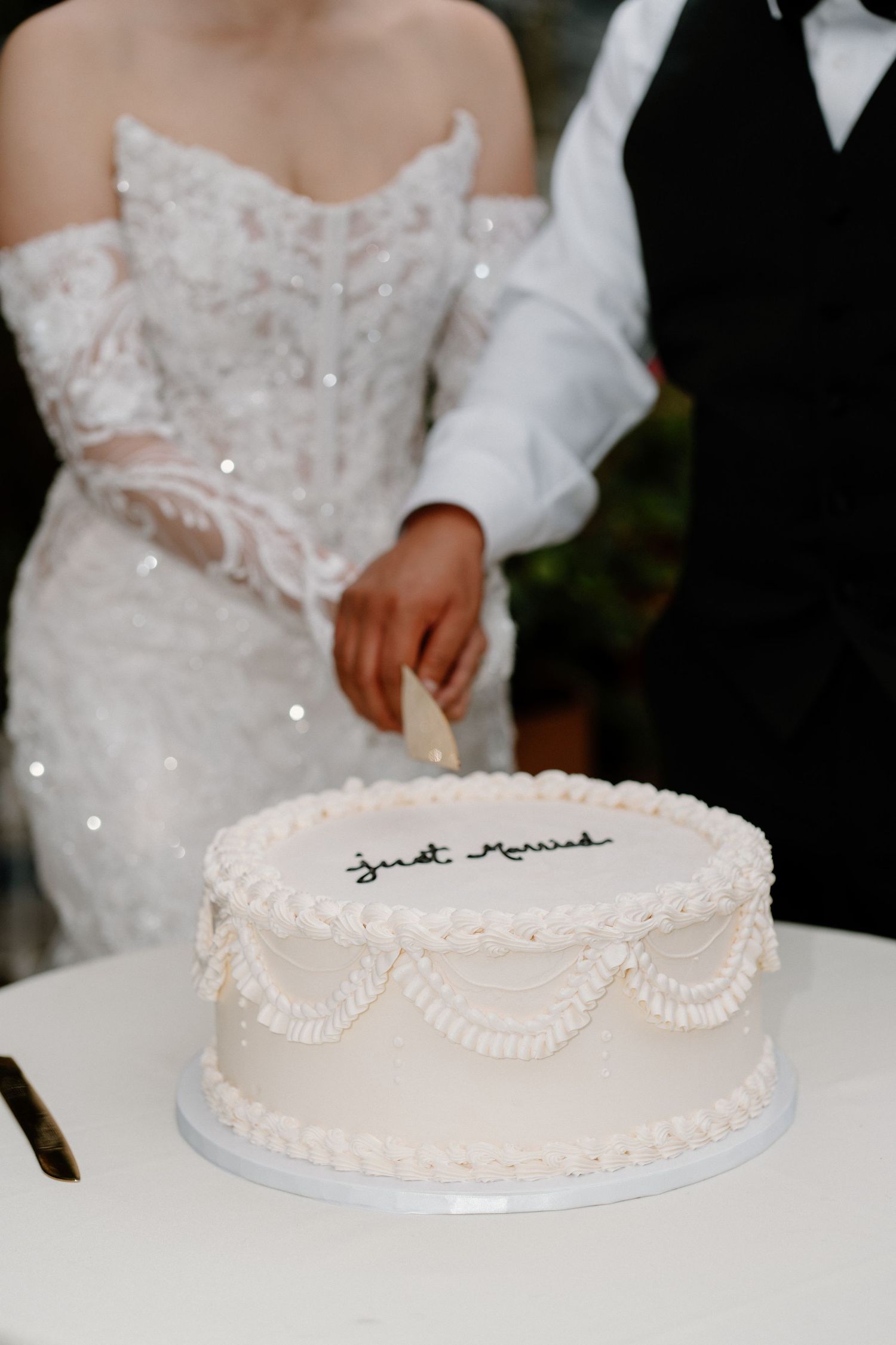Bride and groom cutting white Just Married wedding cake at elegant wedding reception celebration.