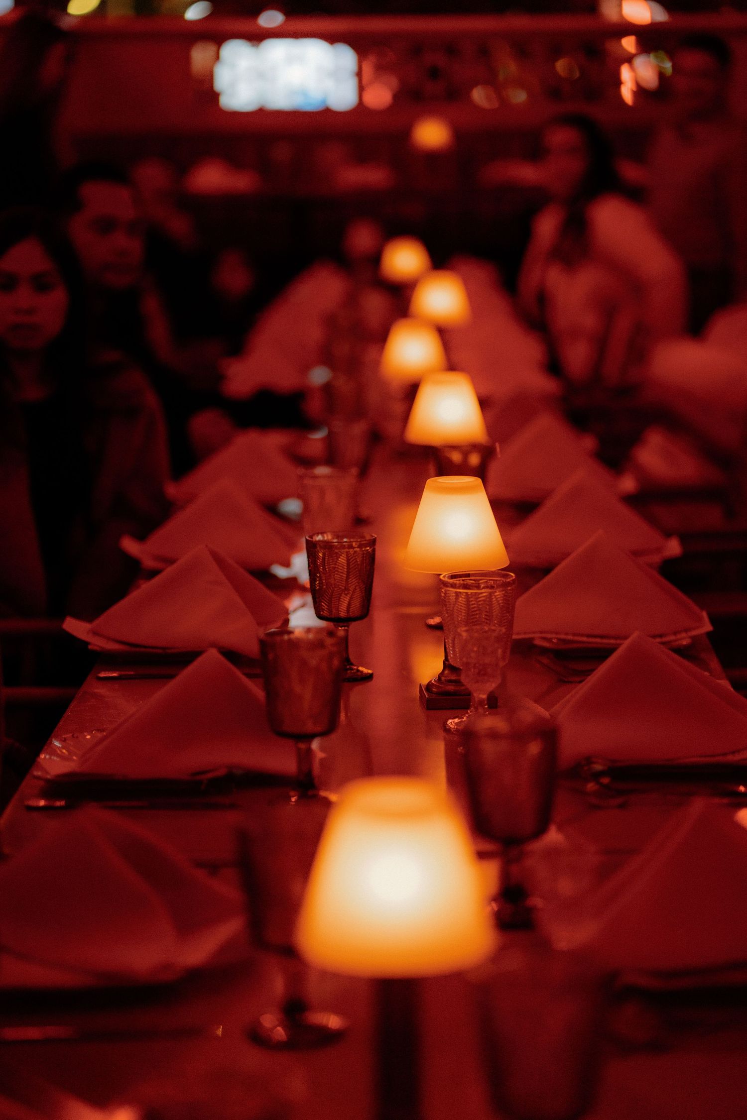 Elegant wedding reception table with glowing candle lamps and red napkins in dim lighting.