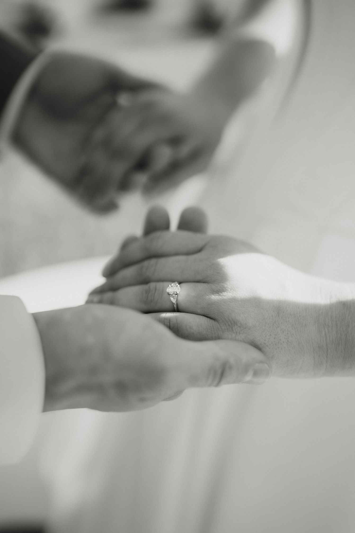 Black and white close-up of bride and groom holding hands showing diamond engagement ring.