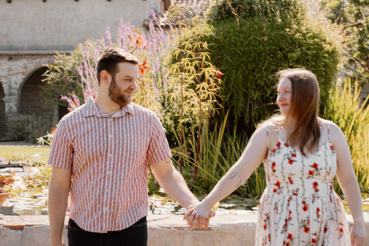 Happy couple holding hands and smiling at each other in a sunny garden setting.