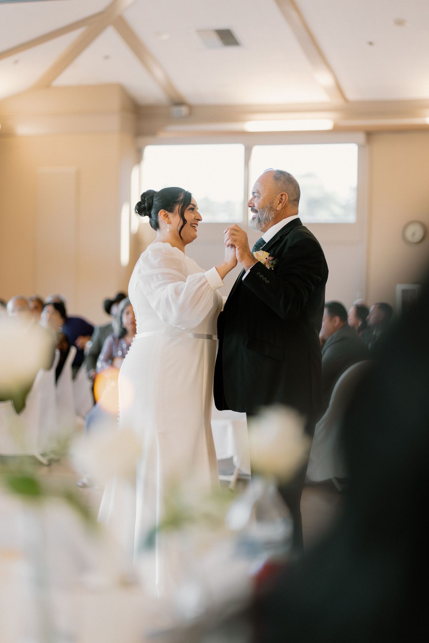 Bride and groom share first dance at wedding reception in elegant white venue.