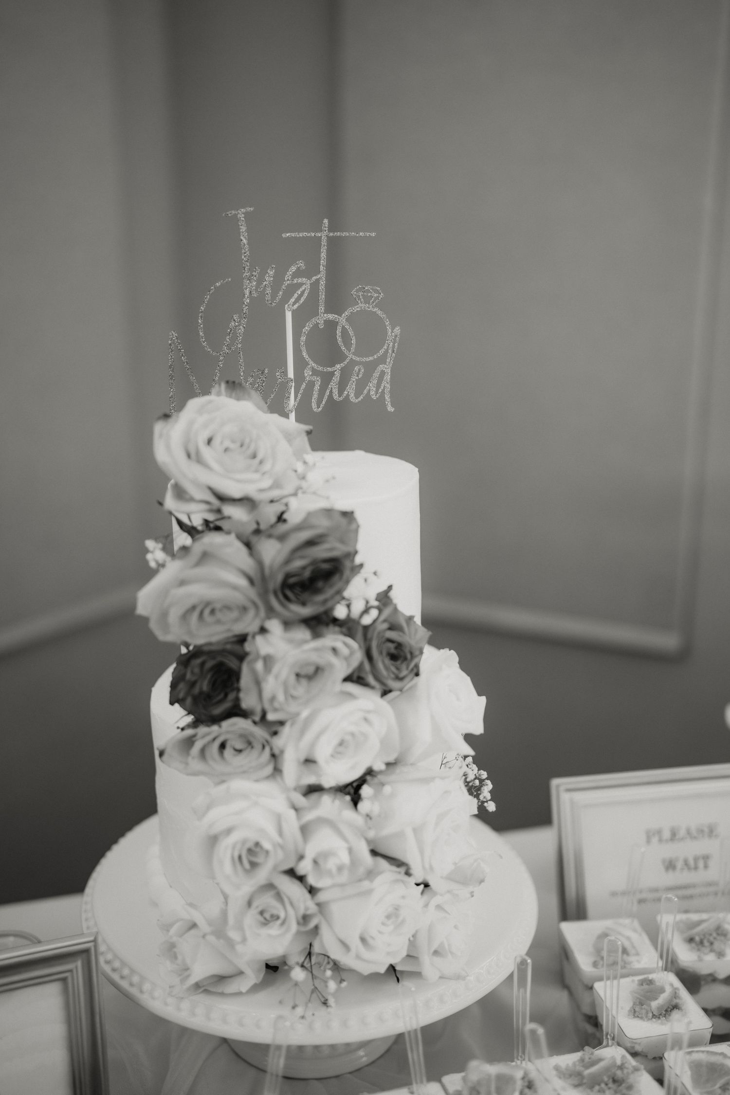 Black and white photo of a two-tier wedding cake with roses and a Just Married topper.