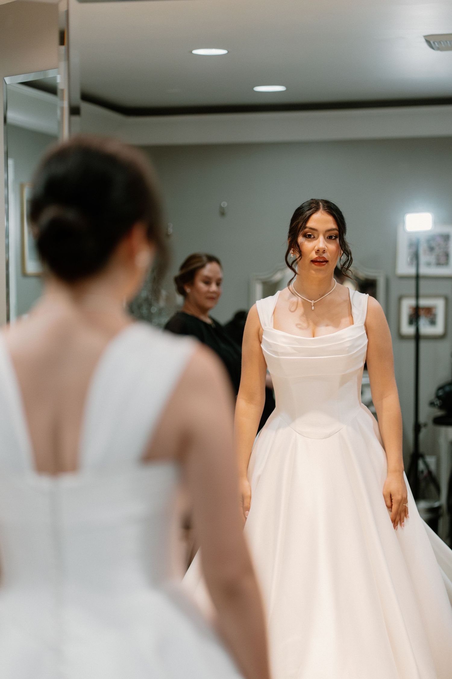 Bride in a white ball gown examining her wedding dress in a bridal boutique mirror fitting room.