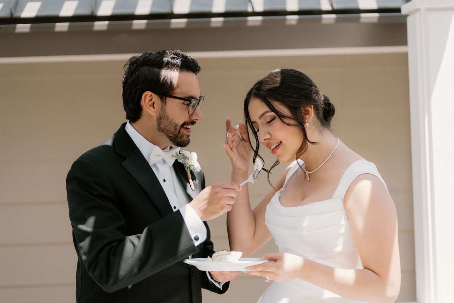 Smiling groom feeds bride a bite of wedding cake during outdoor cake cutting ceremony at their reception.