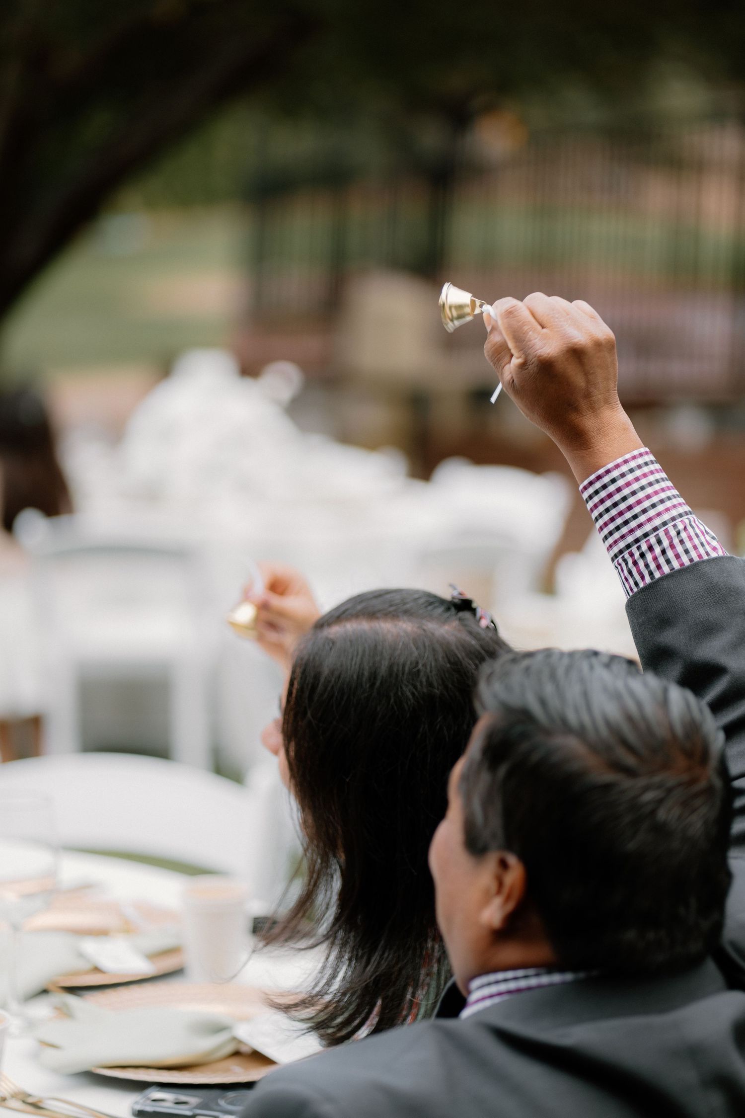 Guest raises a small gold bell at an elegant outdoor wedding reception dinner.