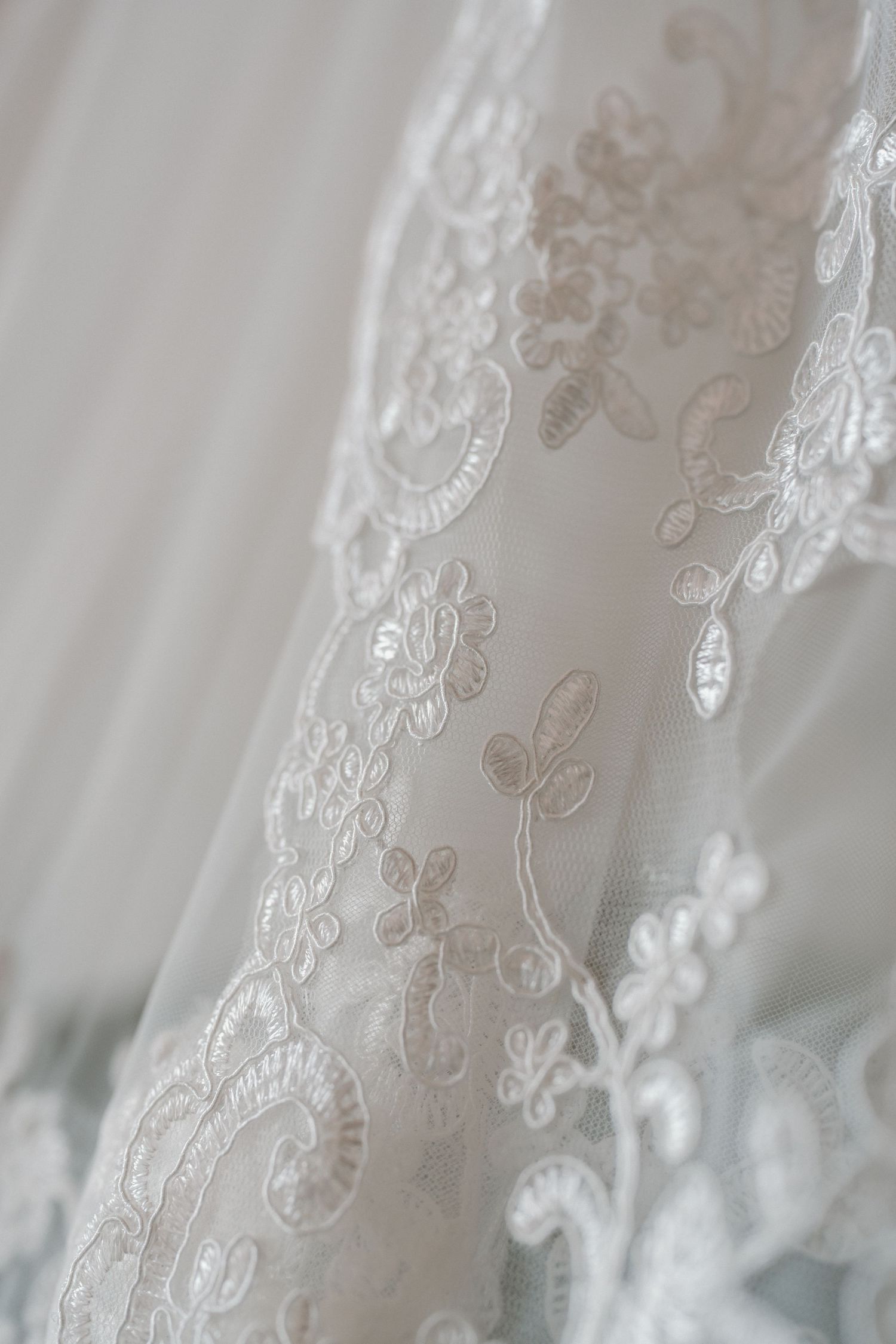 Close-up detail of elegant white lace wedding dress with floral embroidery and sequin accents.