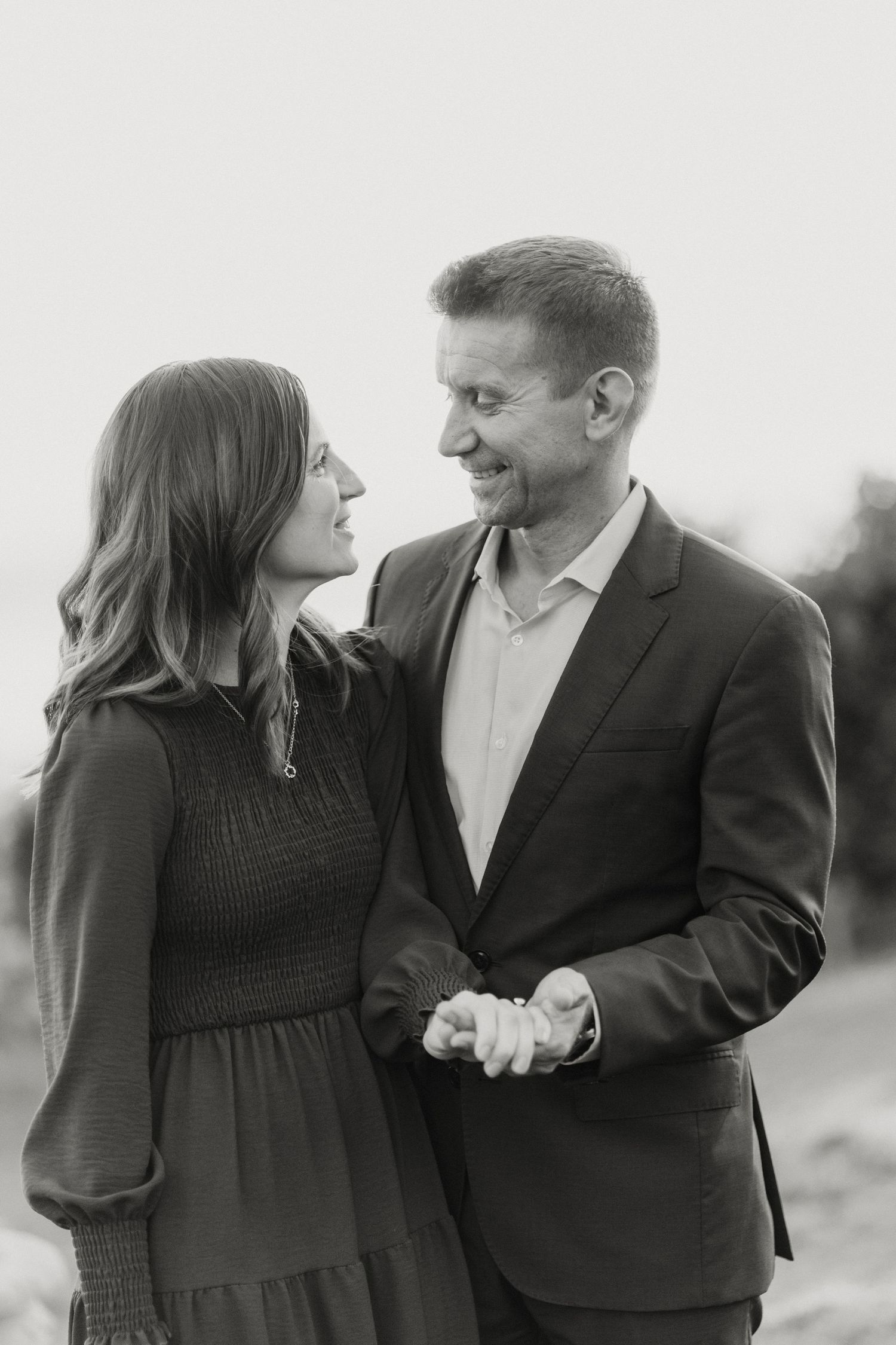 Black and white portrait of smiling couple holding hands and gazing at each other.
