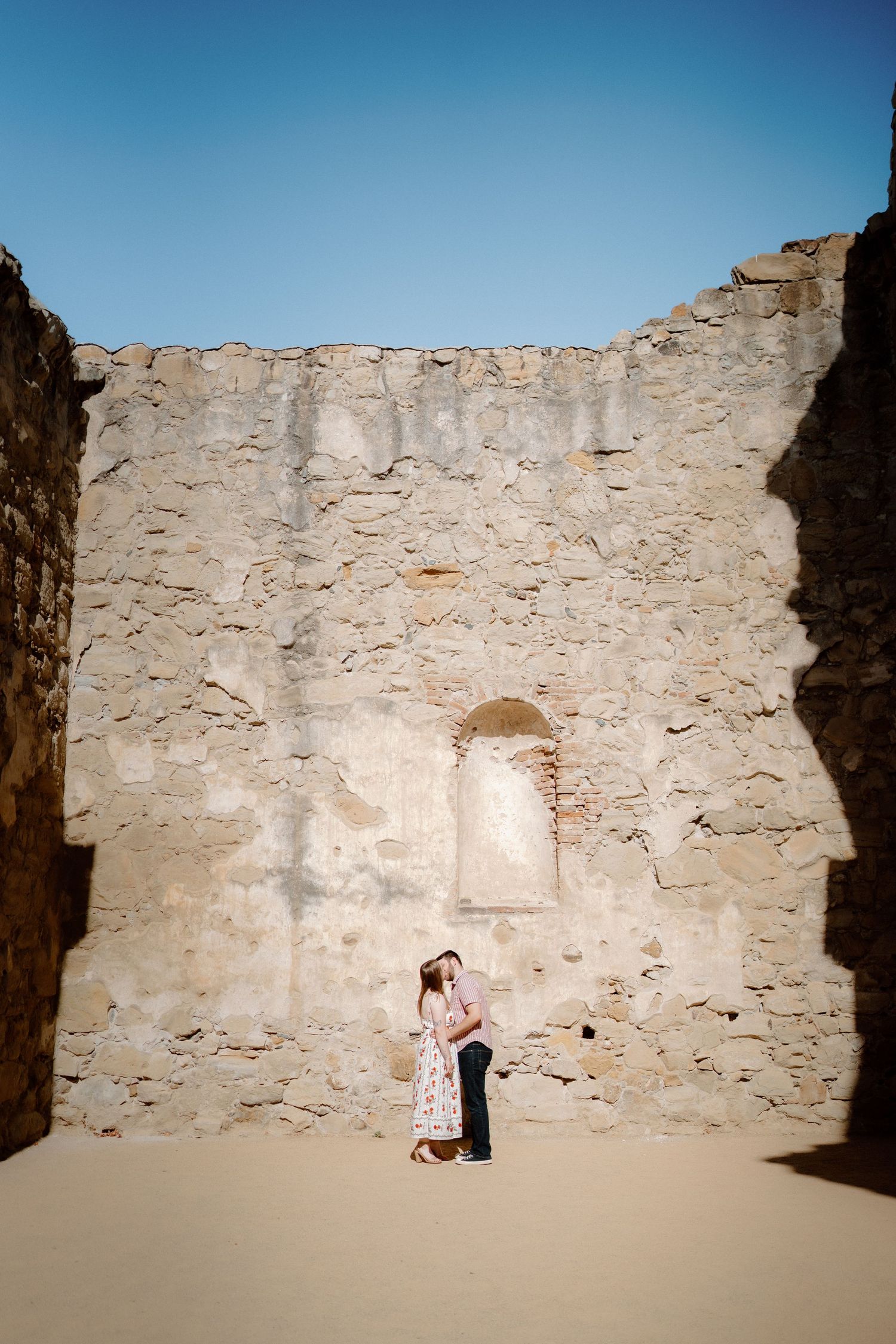 Couple sharing a romantic moment in ancient stone ruins under a clear blue sky.