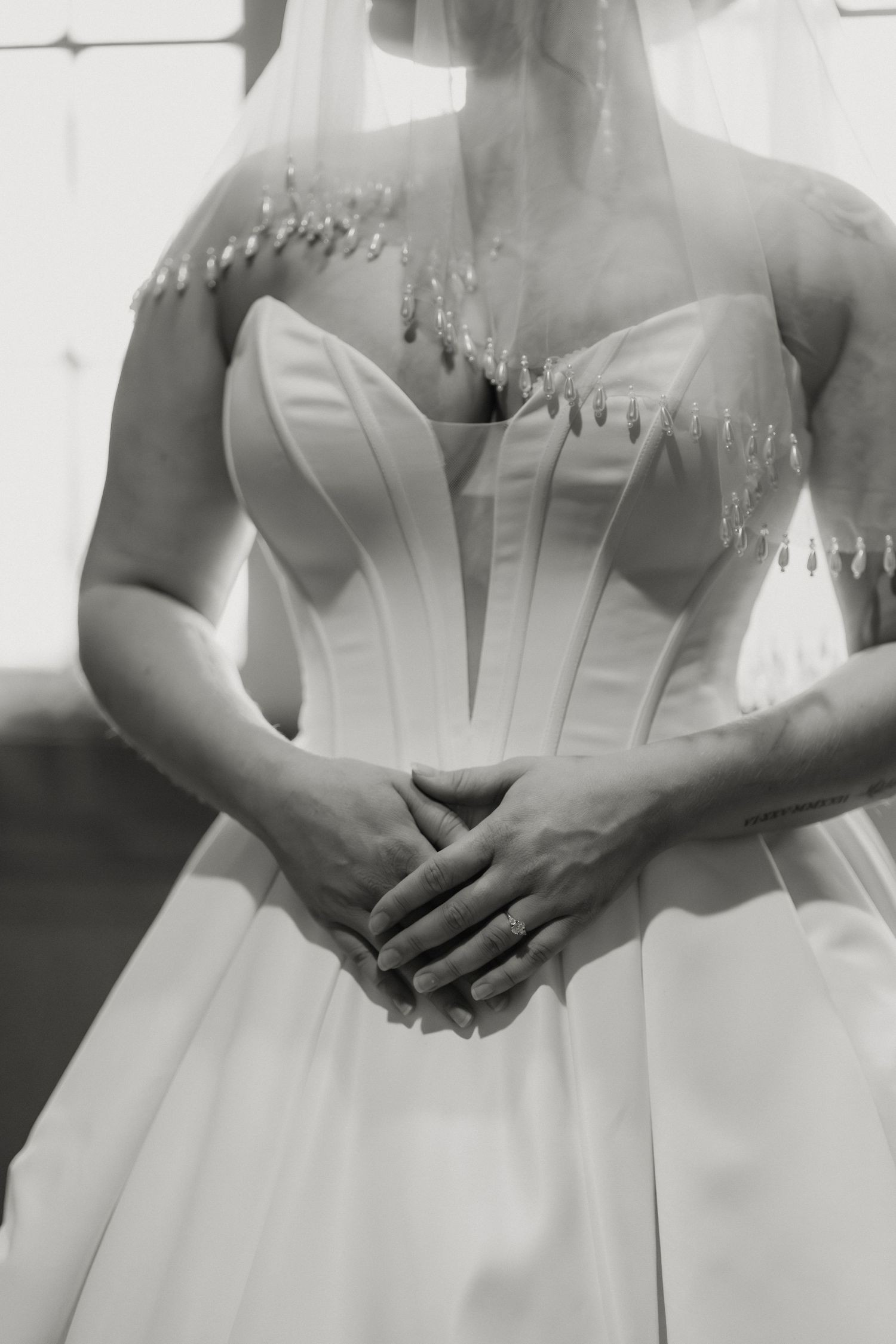 Black and white photo of a bride in a corset wedding dress with groom's arms wrapped around her waist.