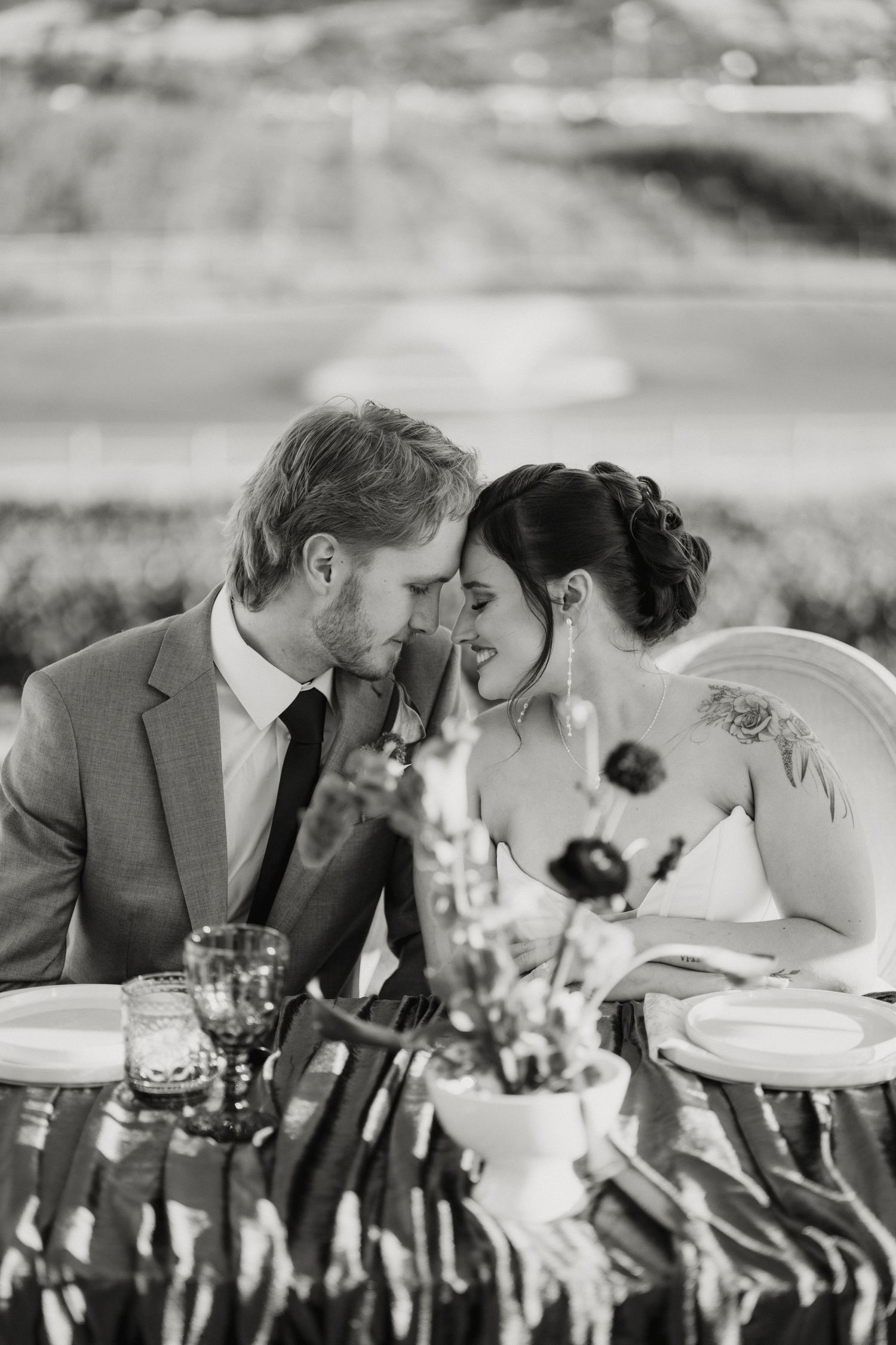 Black and white photo of bride and groom sharing an intimate moment at their wedding reception table.