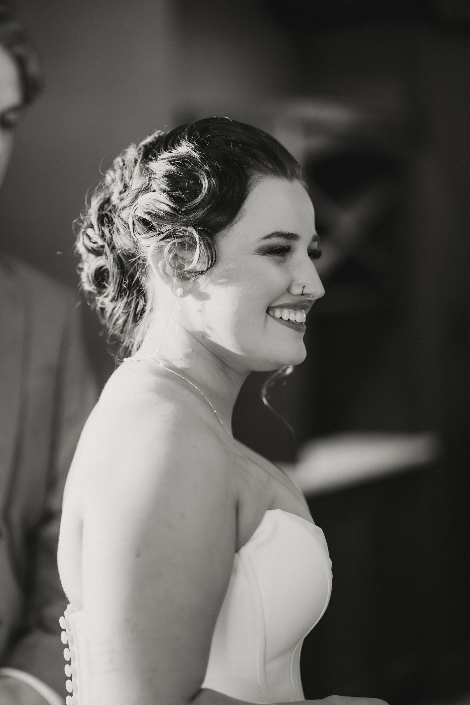 Black and white photo of a smiling bride in a strapless gown with elegant updo hairstyle on her wedding day.