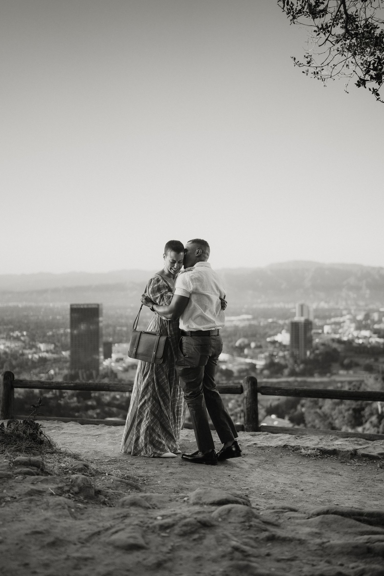 Black and white photo of a couple embracing after a proposal at a scenic city overlook.