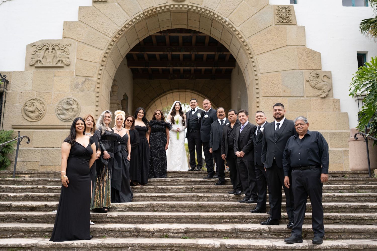 Wedding party in all-black attire posing on stone steps of ornate church entrance.