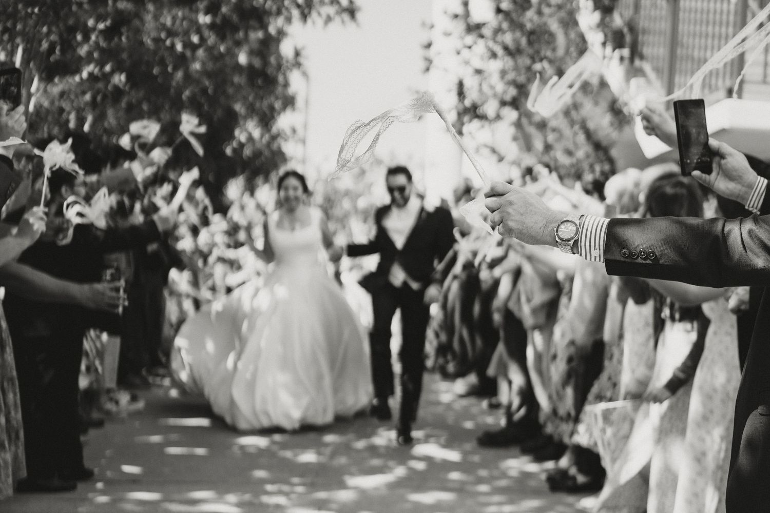 Black and white photo of newlyweds exiting wedding ceremony through cheering guests with streamers.