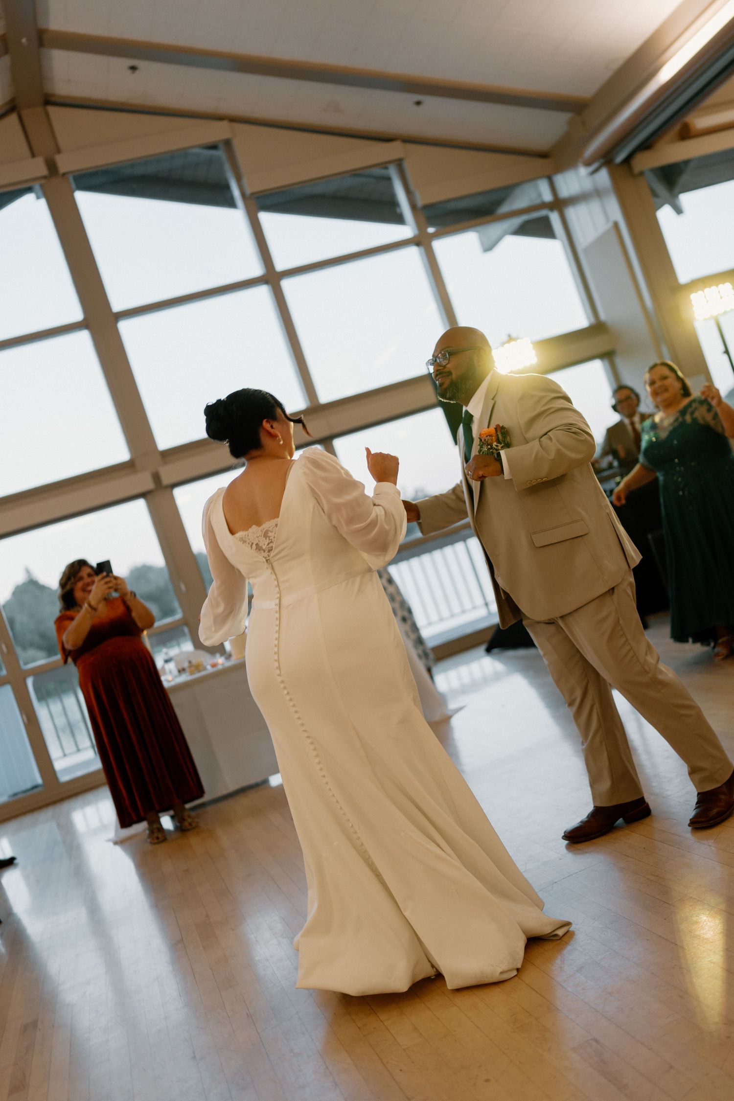 Bride and groom share first dance in sunlit modern reception venue with large windows.