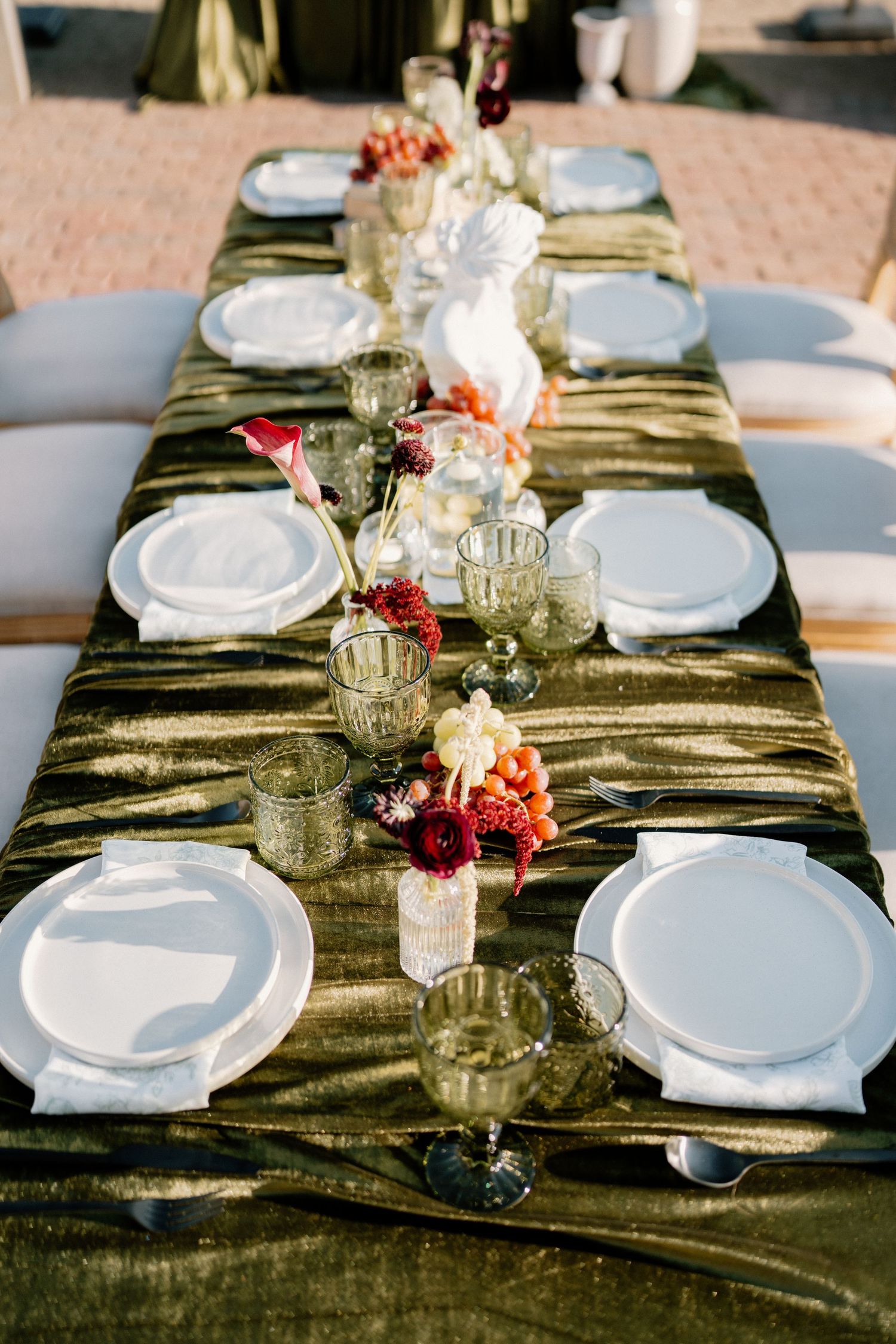 Elegant wedding reception table set with white plates, floral centerpieces, and olive green velvet runner.