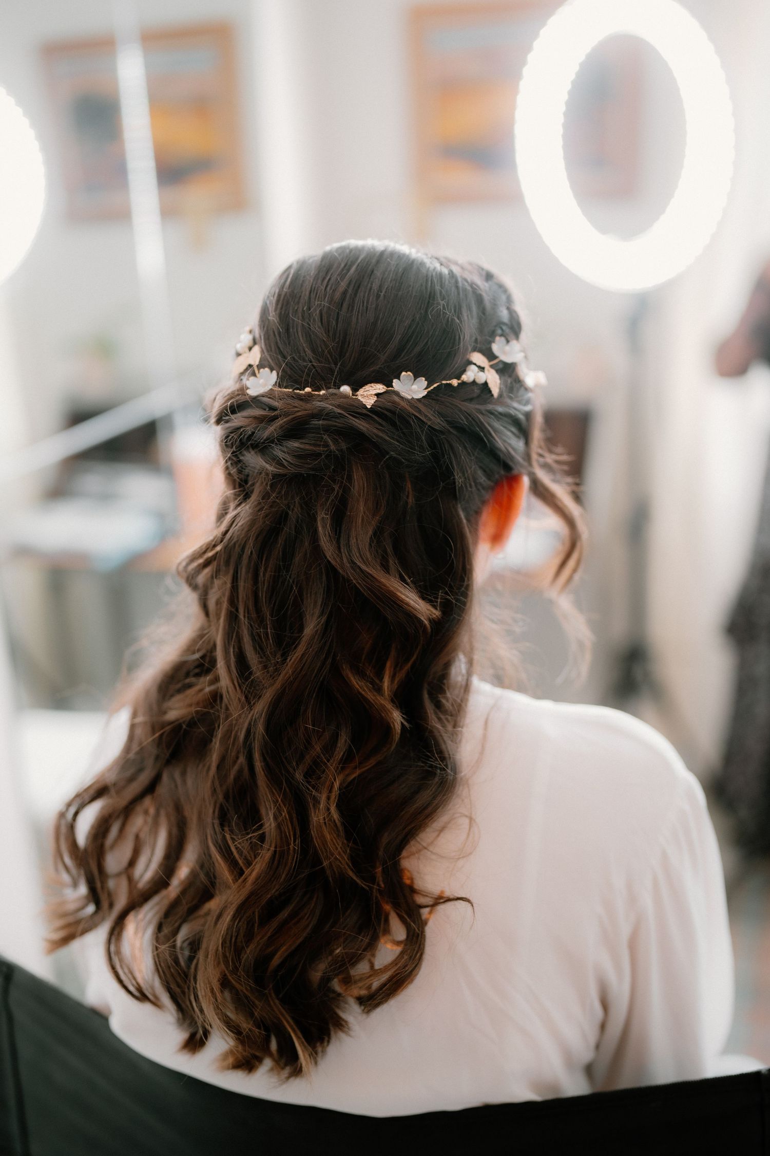 Back view of bride with elegant half-up hairstyle adorned with delicate floral hair vine accessory.