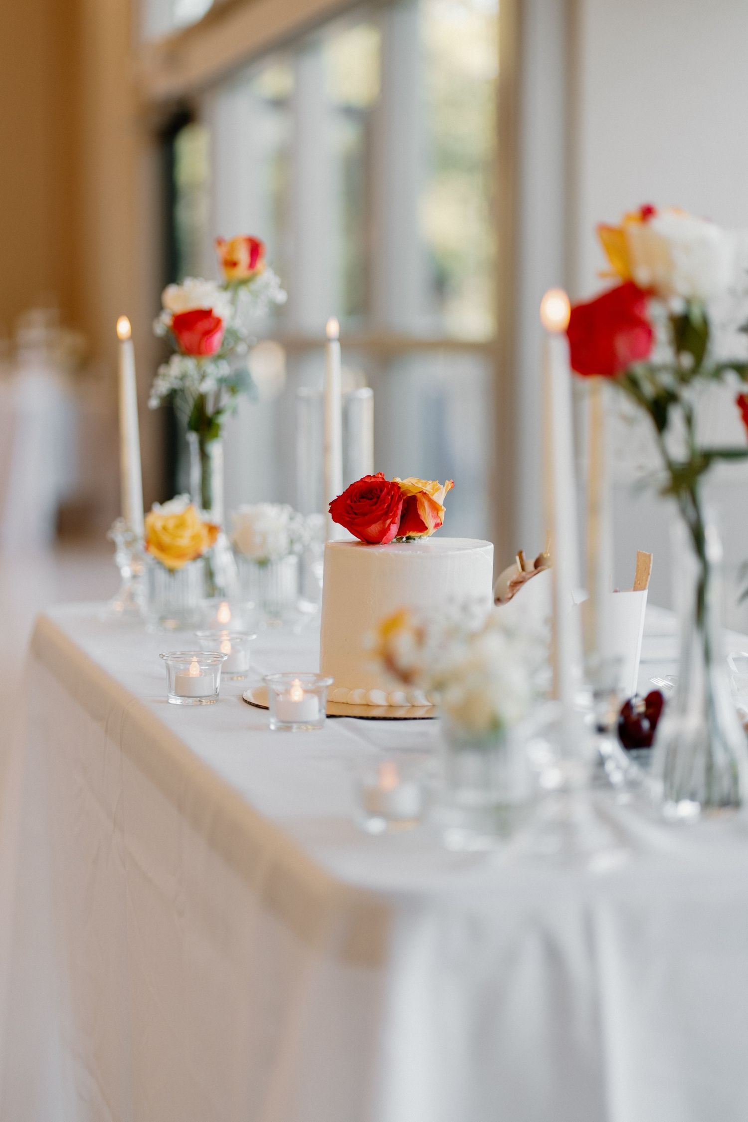 Elegant wedding reception table with white cake, red roses, candles, and floral arrangements.