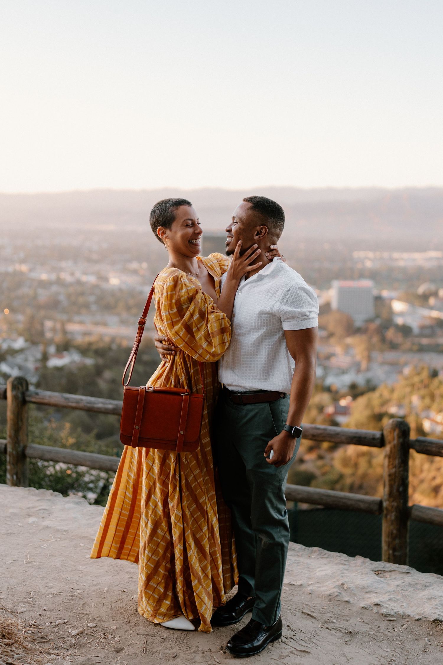 Couple sharing a romantic moment at a scenic overlook with city views and mountains at sunset.