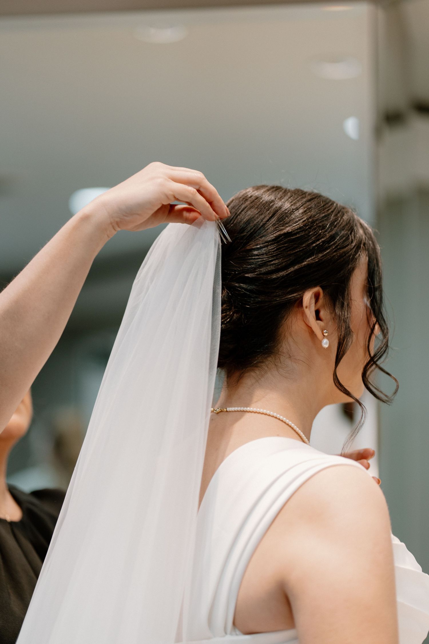 Bridesmaid carefully attaches veil to brides elegant updo hairstyle during bridal preparations before the wedding ceremony.