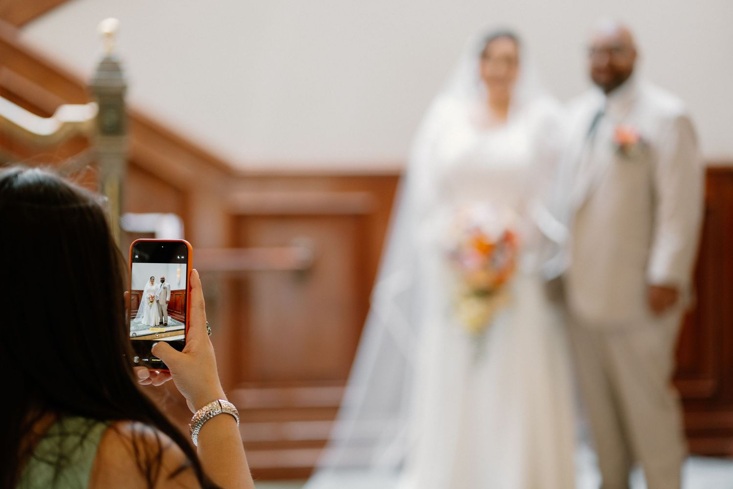 Guest photographs bride and groom at wedding altar using smartphone, capturing couple in white chapel.