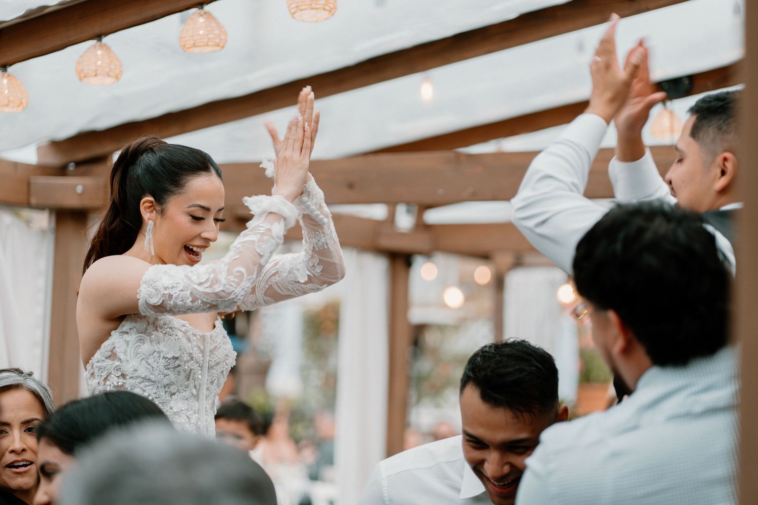 Bride in lace gown high-fiving guests enthusiastically during lively outdoor wedding reception celebration.