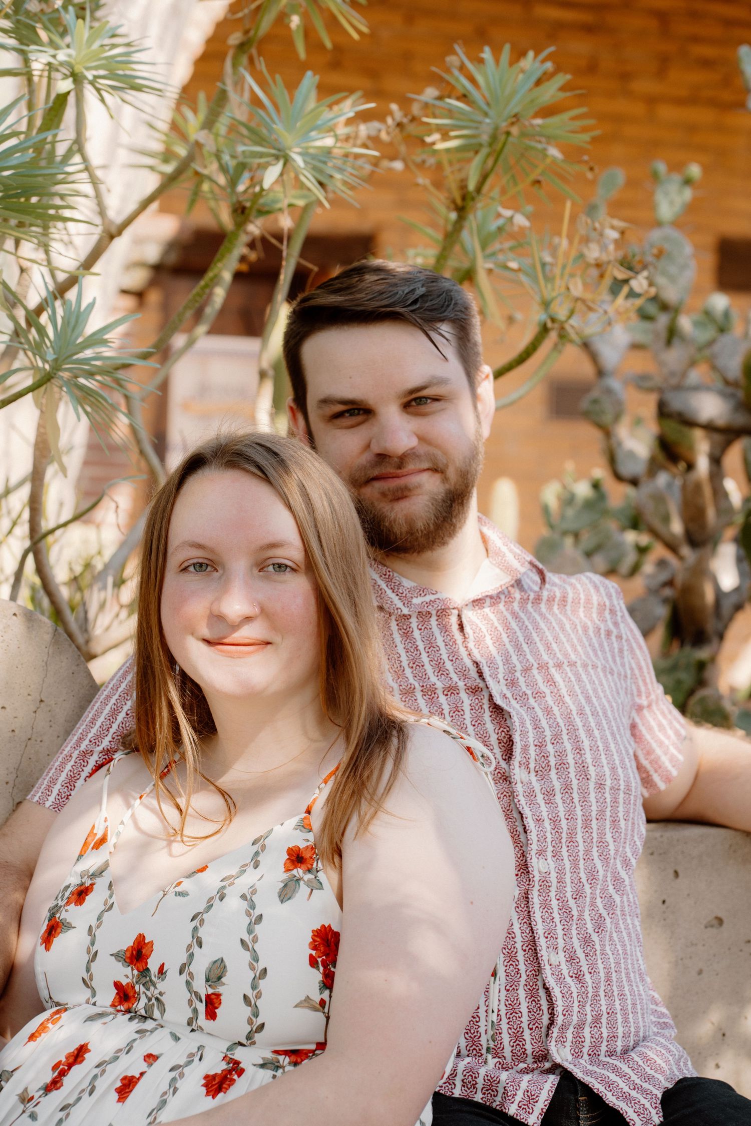 A smiling couple poses together outdoors near cacti and succulents in warm sunlight.