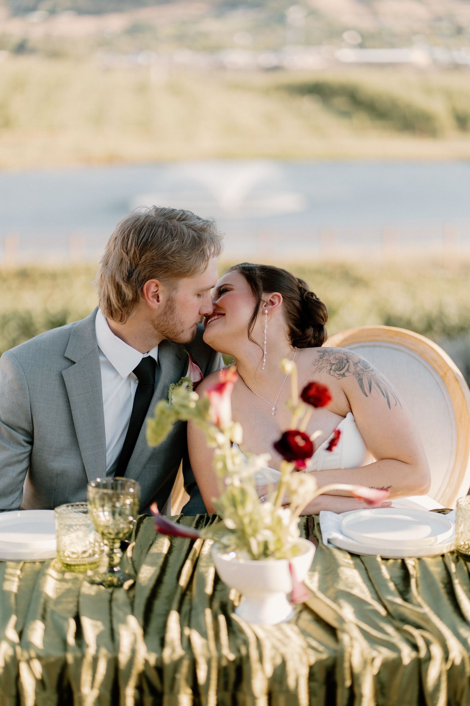 Bride and groom sharing a kiss at outdoor sweetheart table with floral decor.