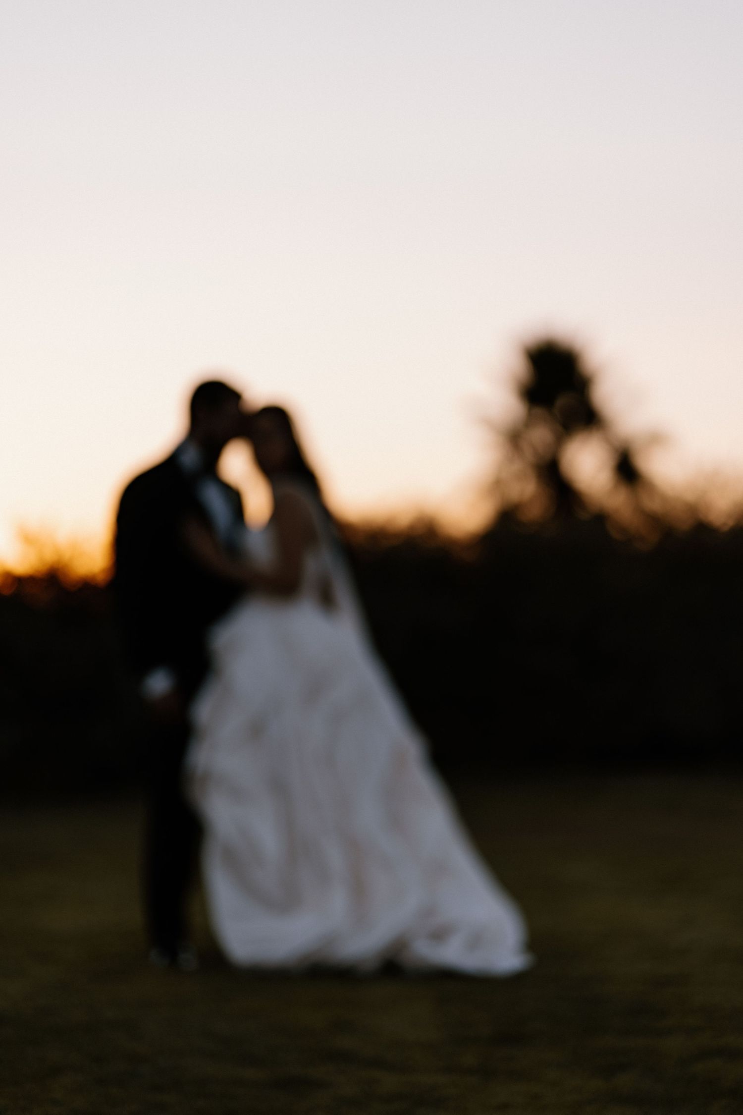Silhouette of bride and groom sharing intimate sunset moment in golden evening light.